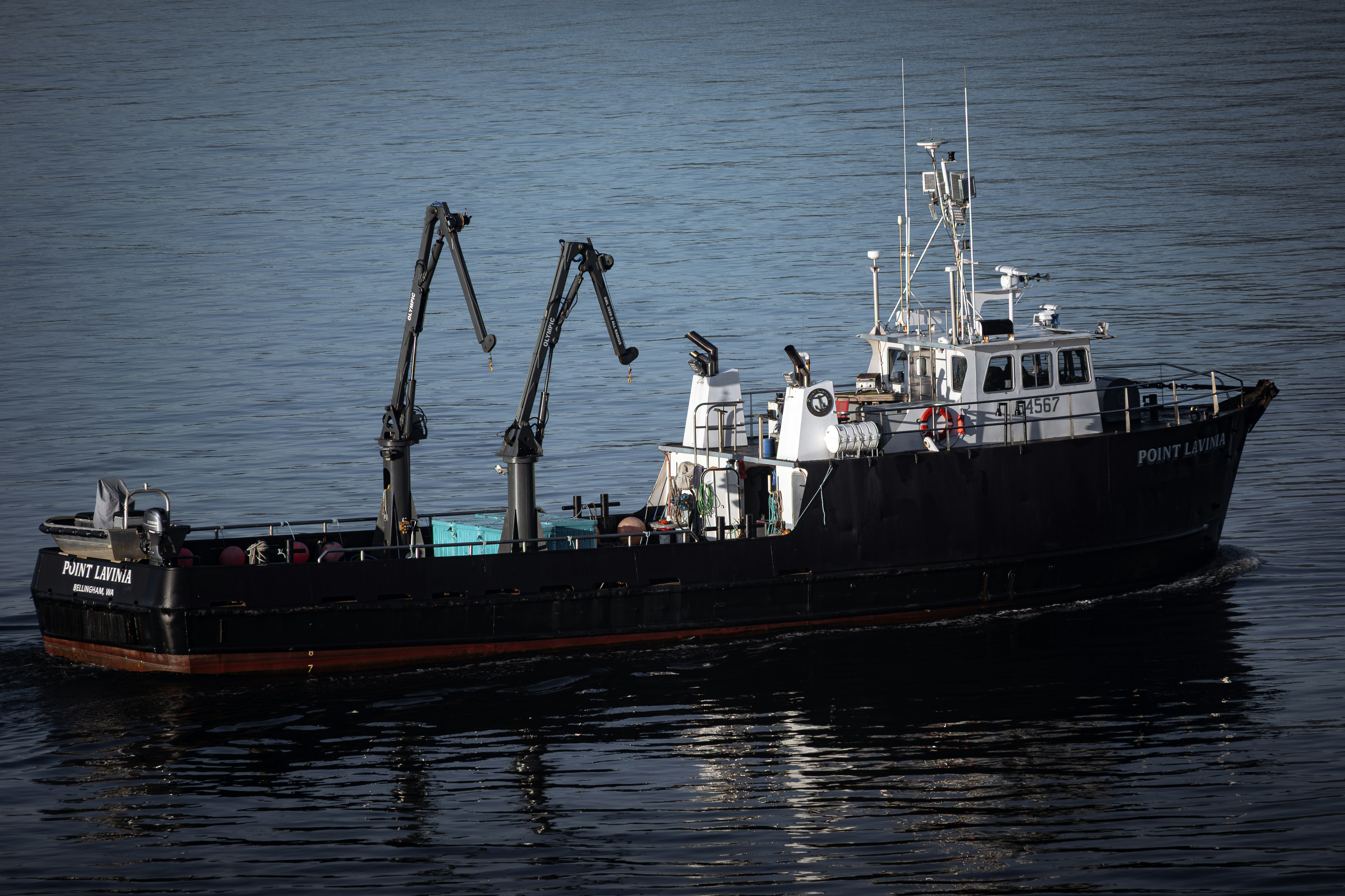 Un bateau de pêche sombre avec des grues navigue sur une eau calme.