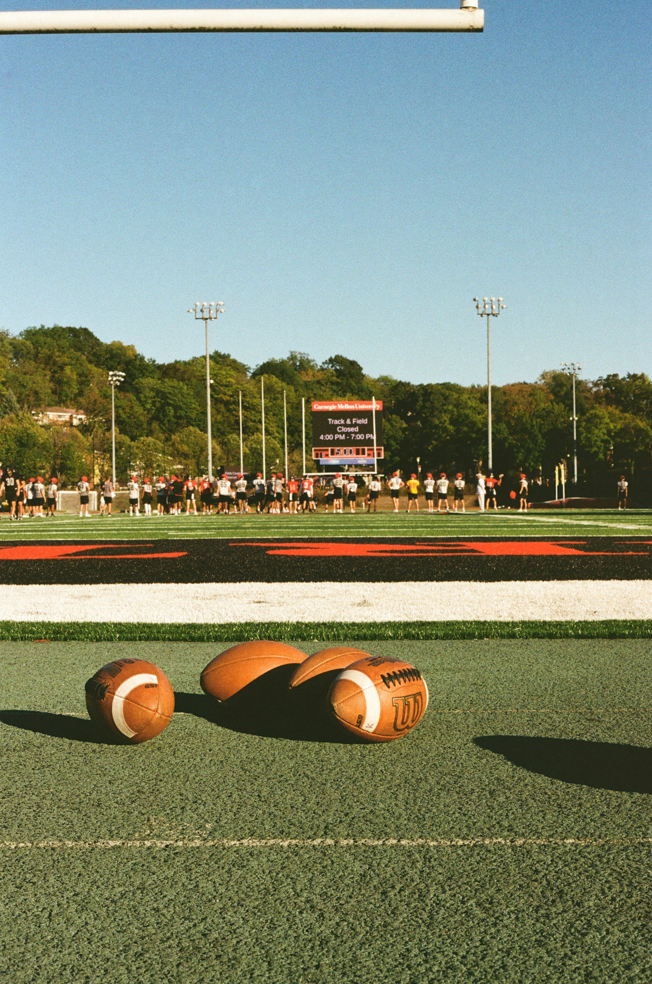 Three footballs on a green field with players in background.
