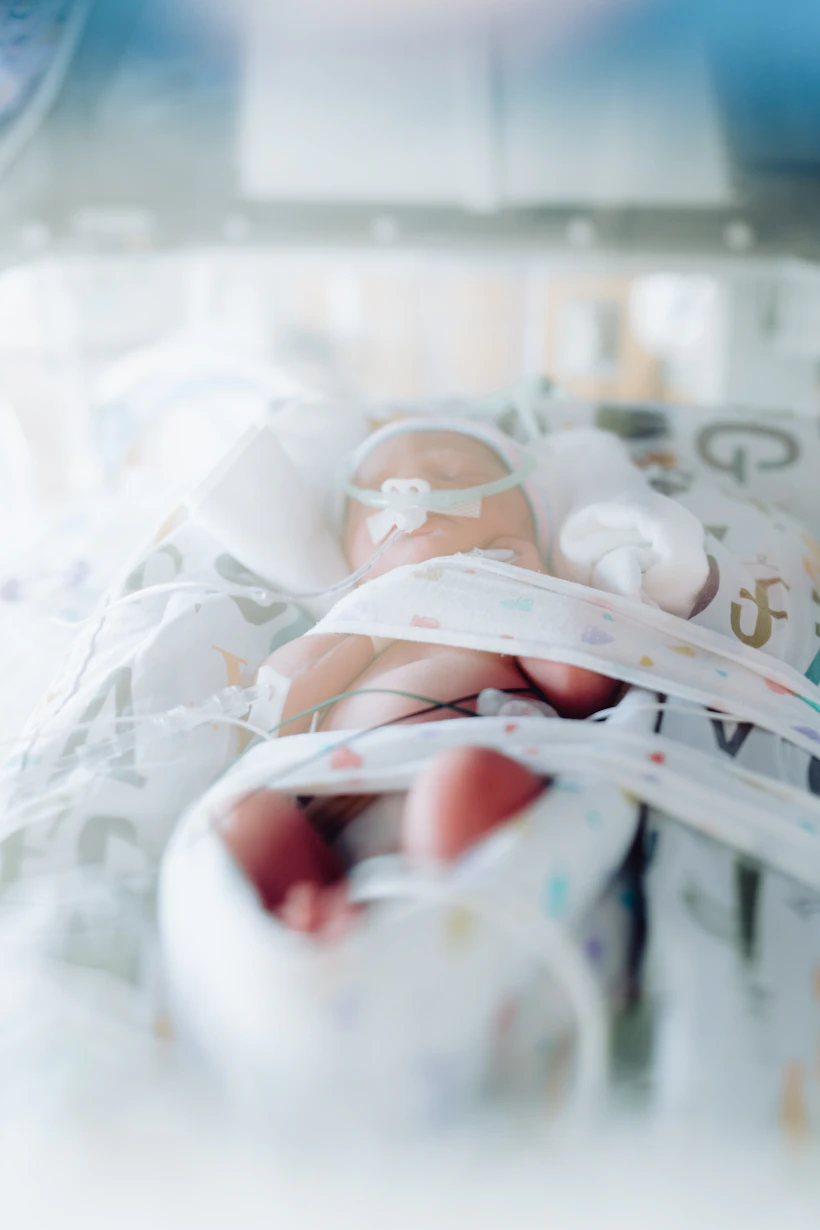Premature infant's hand inside a neonatal intensive care unit incubator with monitoring leads attached