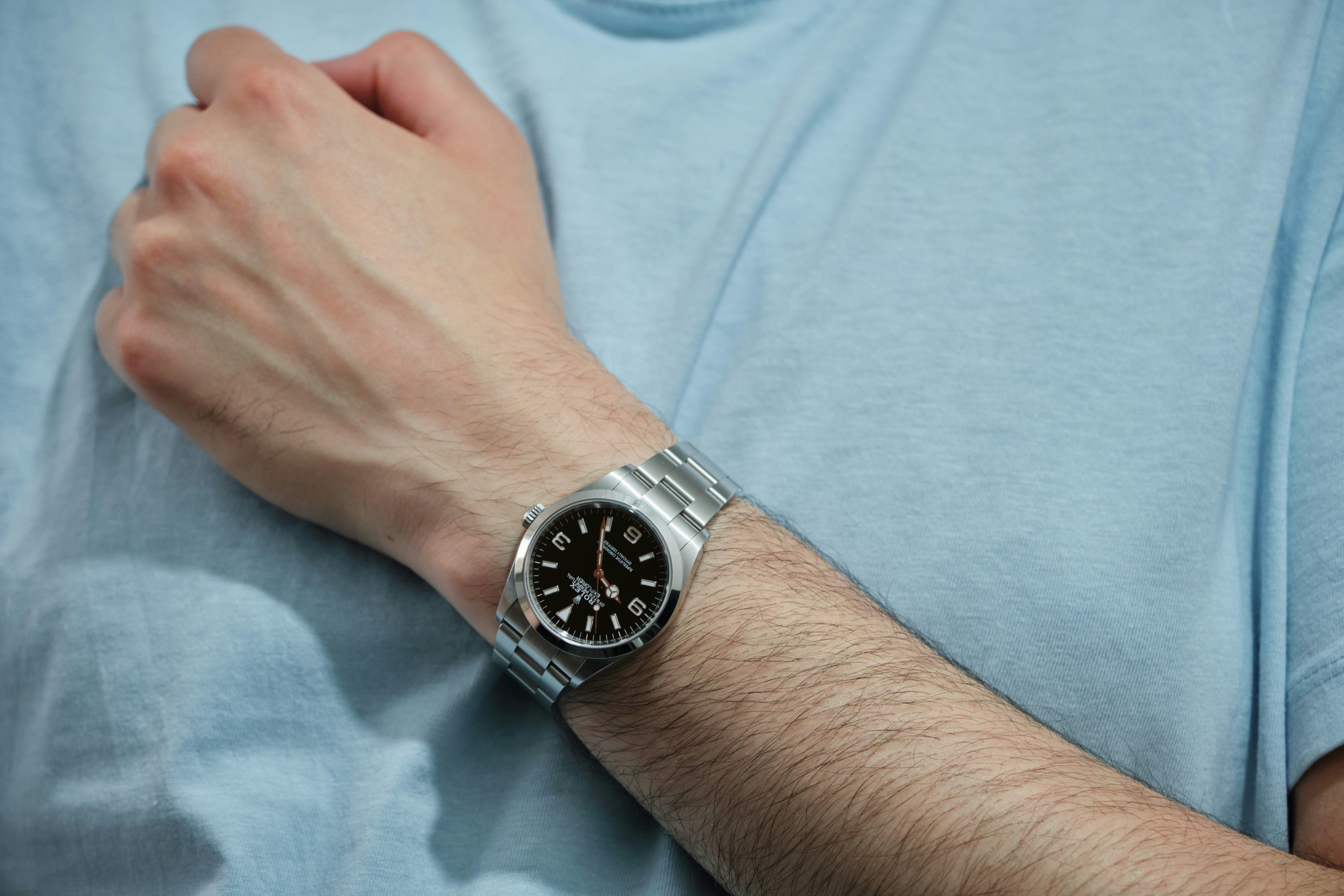 Wrist wearing a silver watch on a light blue shirt.