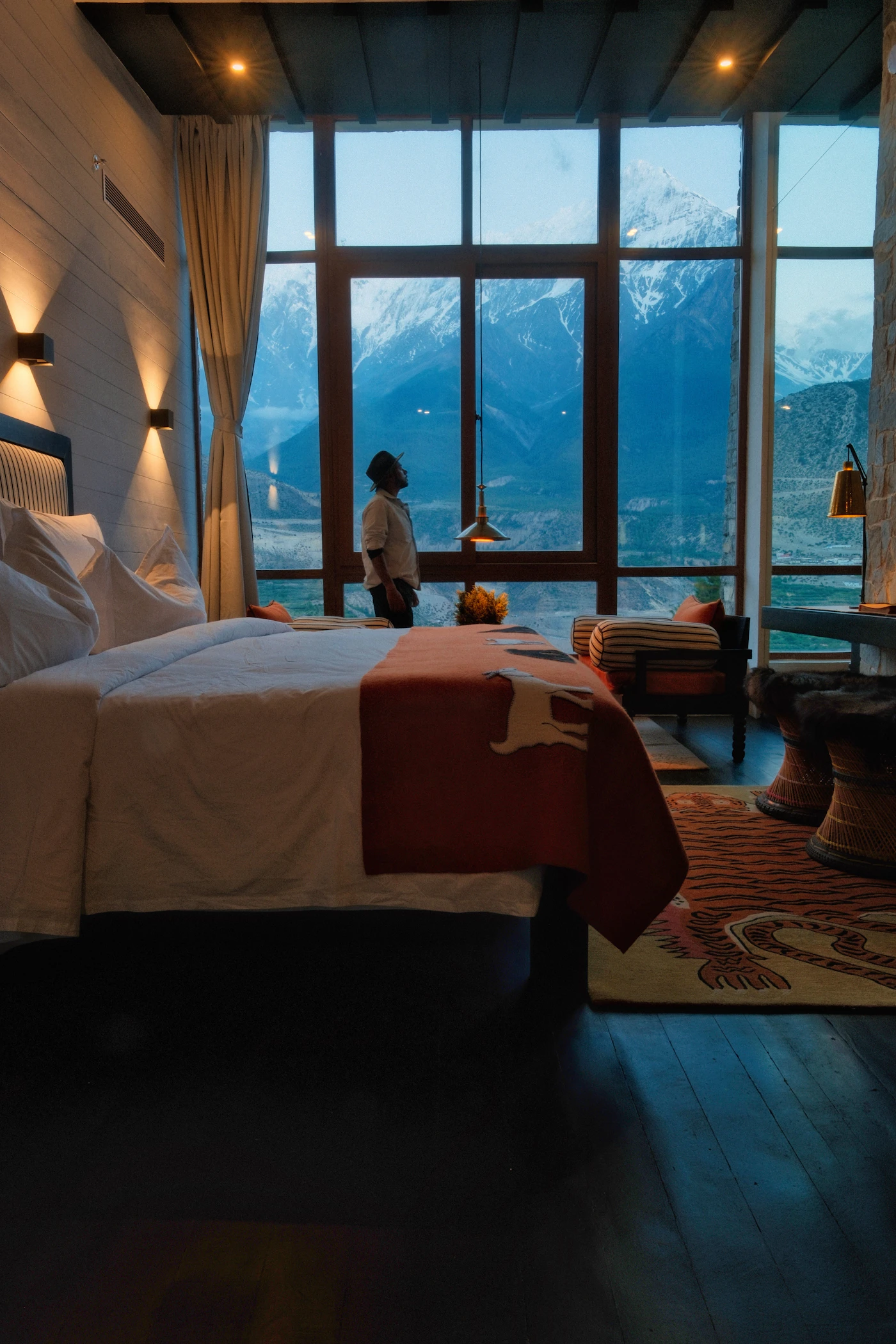 A traveller looking out floor-to-ceiling hotel windows at snowy mountains