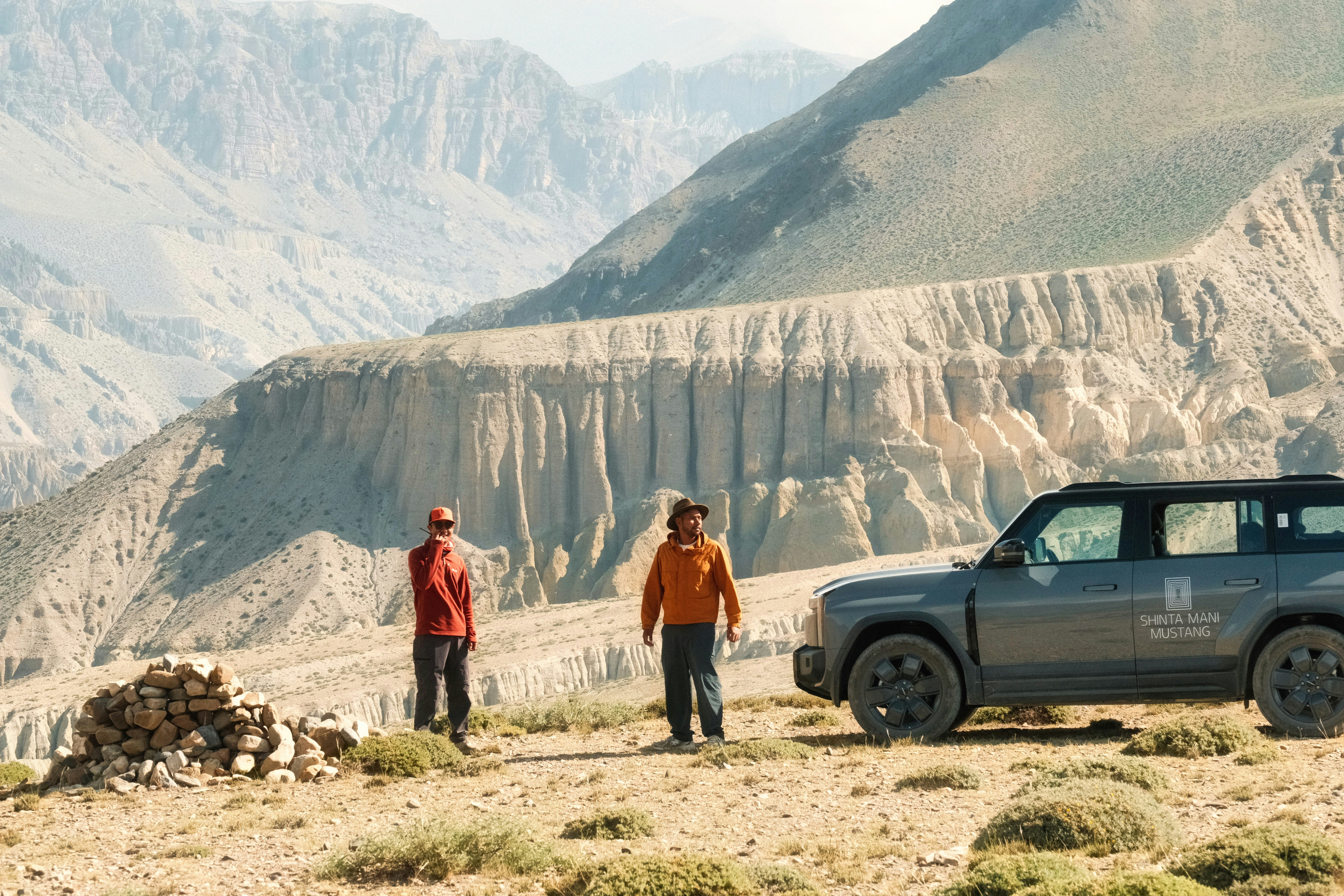 Two people and an suv in a rugged mountain landscape