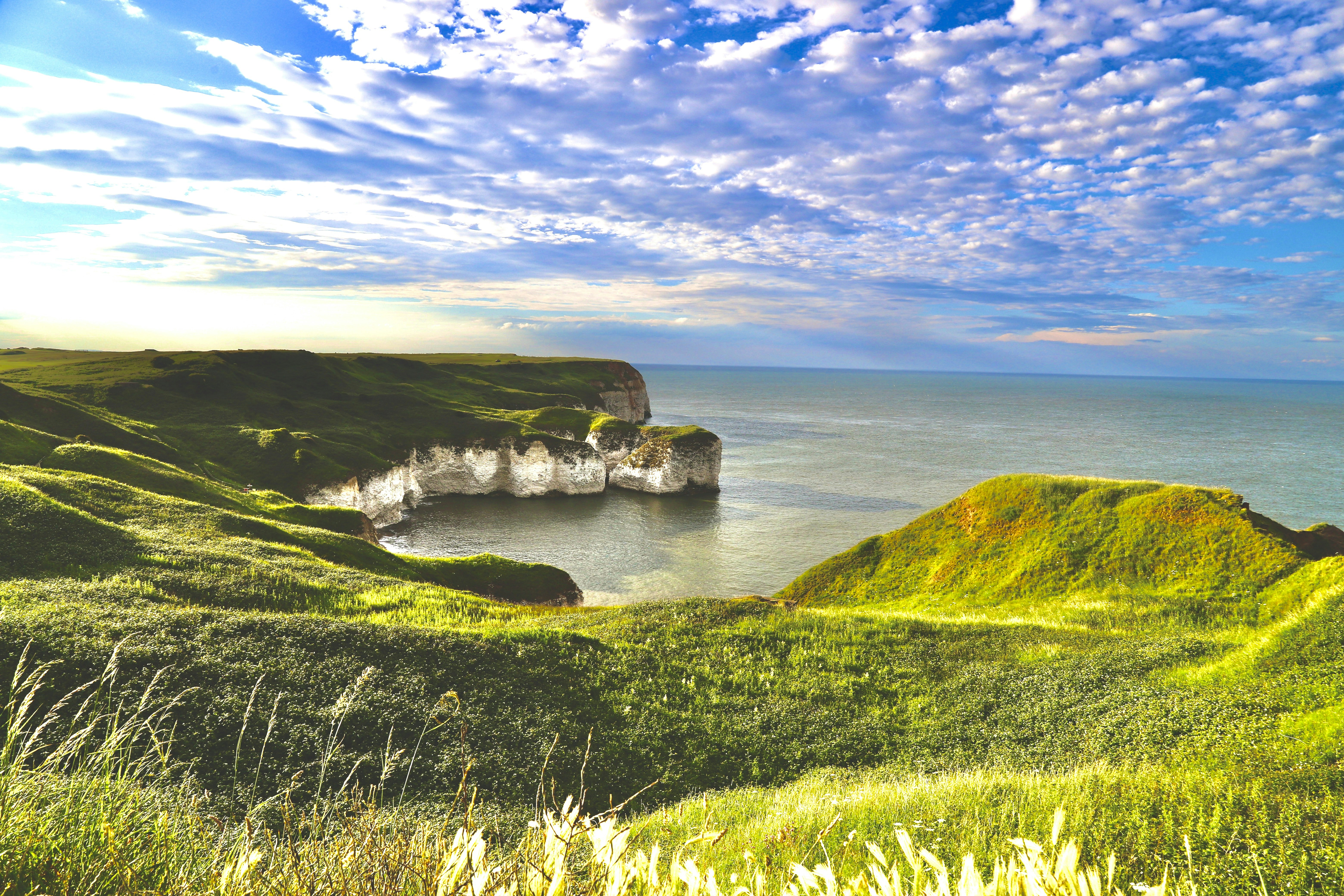 Lush green cliffs meet the ocean under a blue sky.