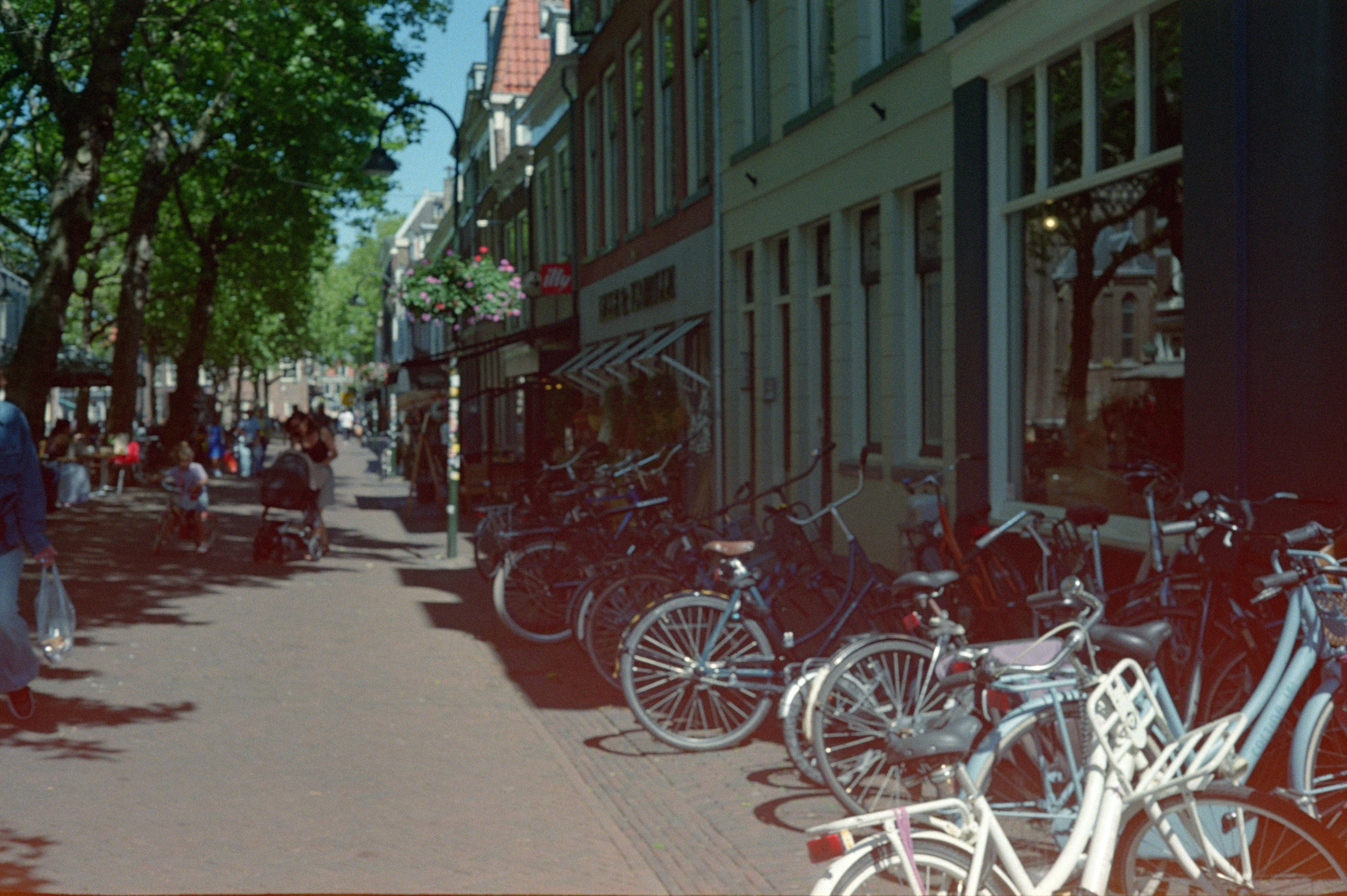 Bicycles parked along a sunny street with people walking.