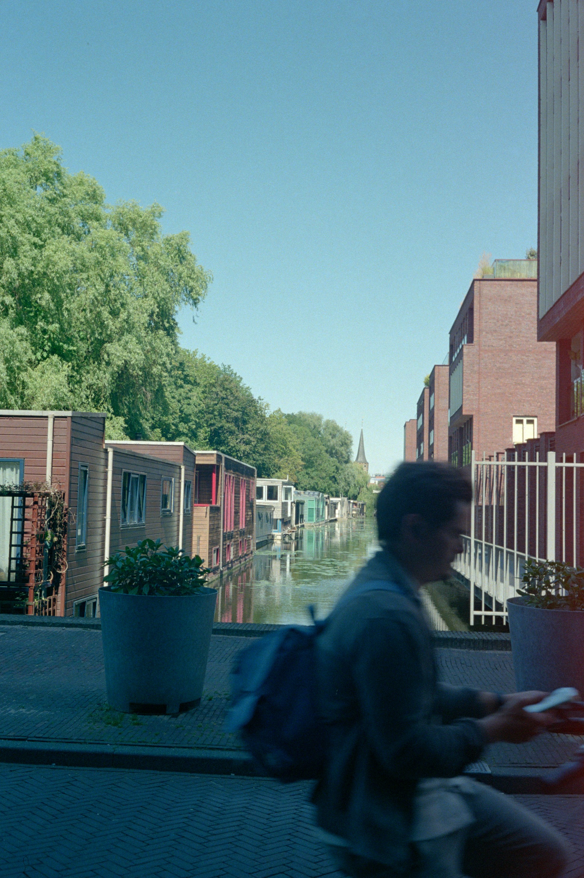 Cyclist rides past houseboats on a sunny canal.