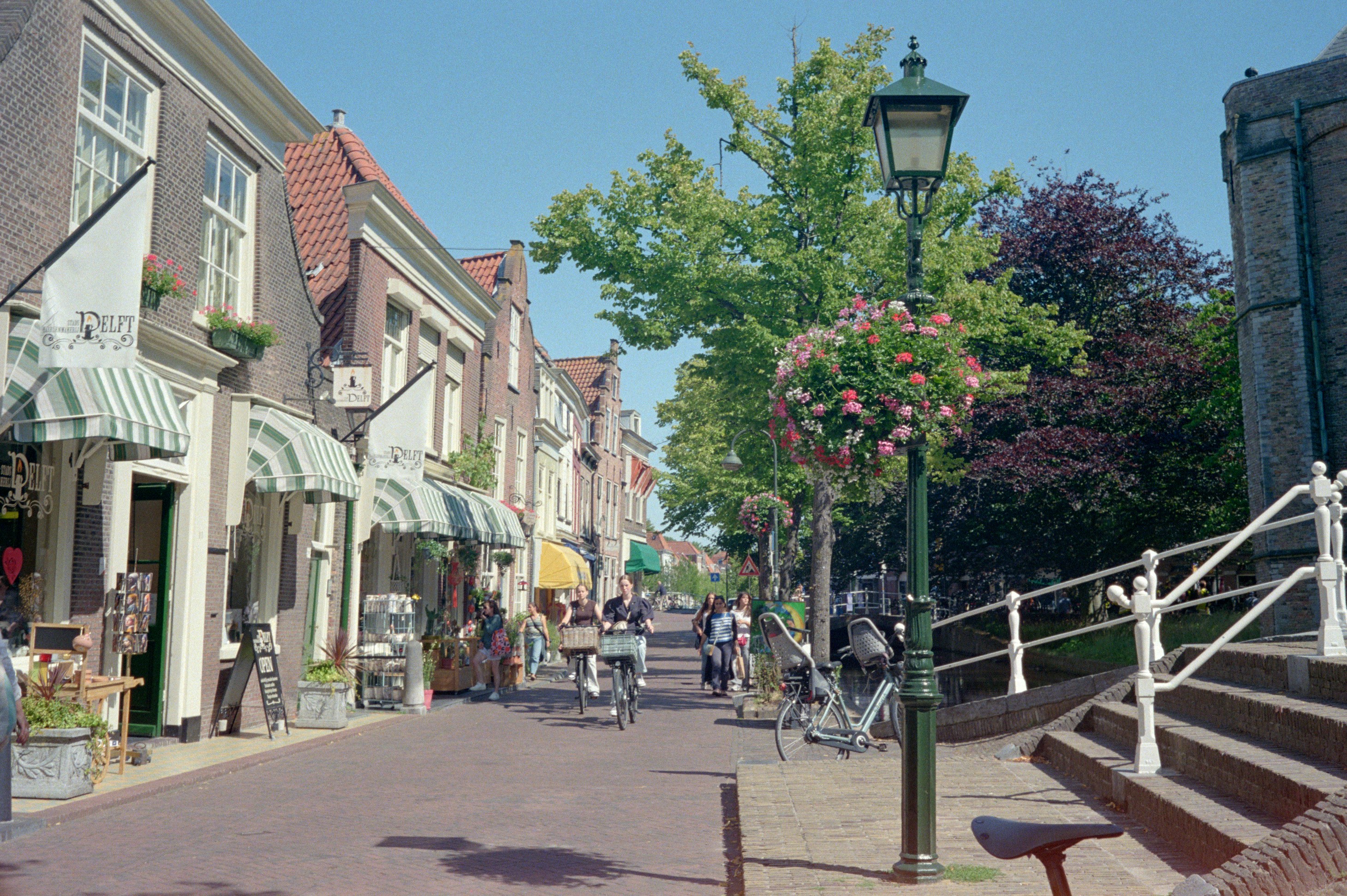 People walk and cycle along a charming street with shops.