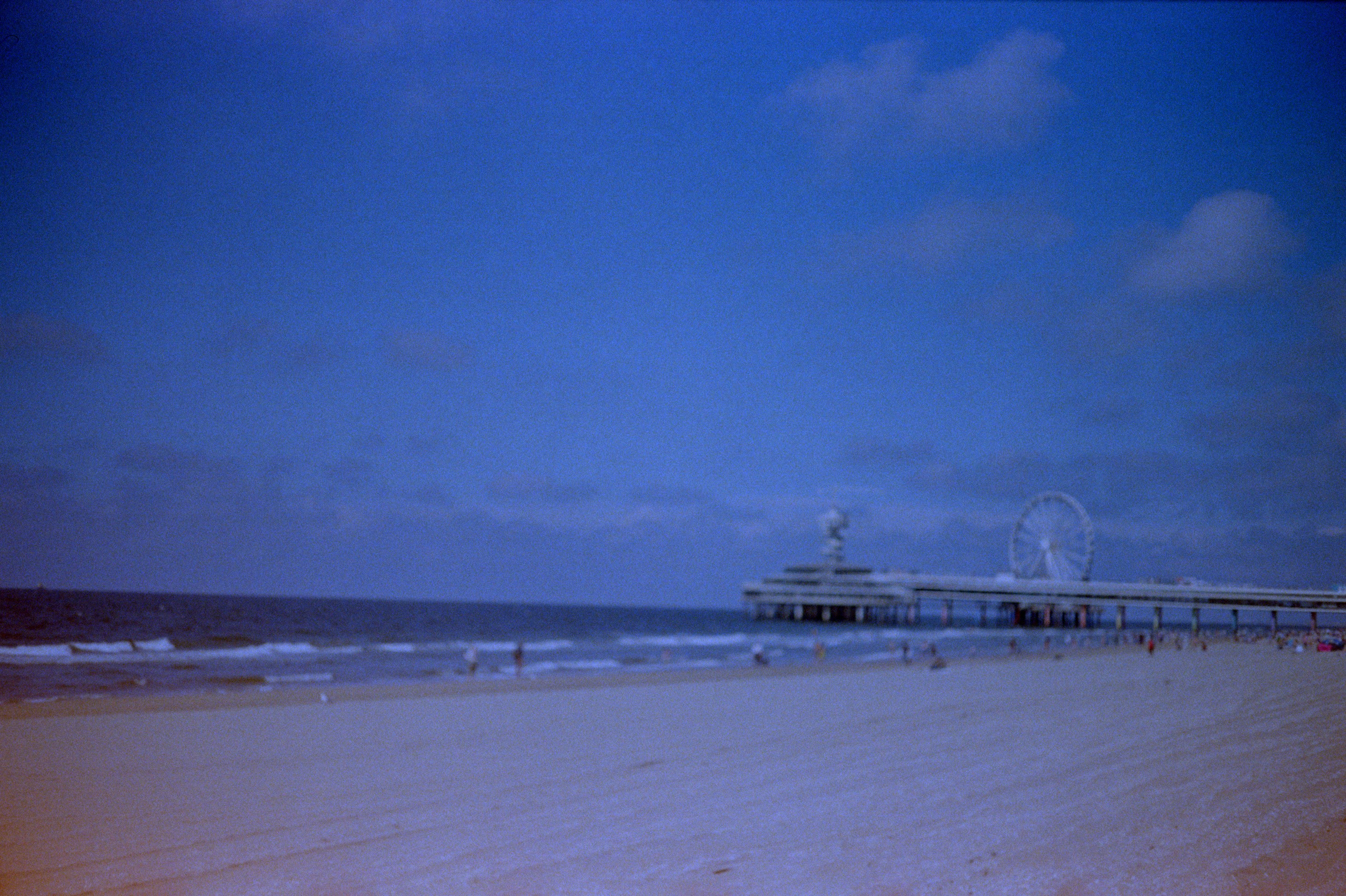 Sandy beach, ocean, and pier under a cloudy sky.