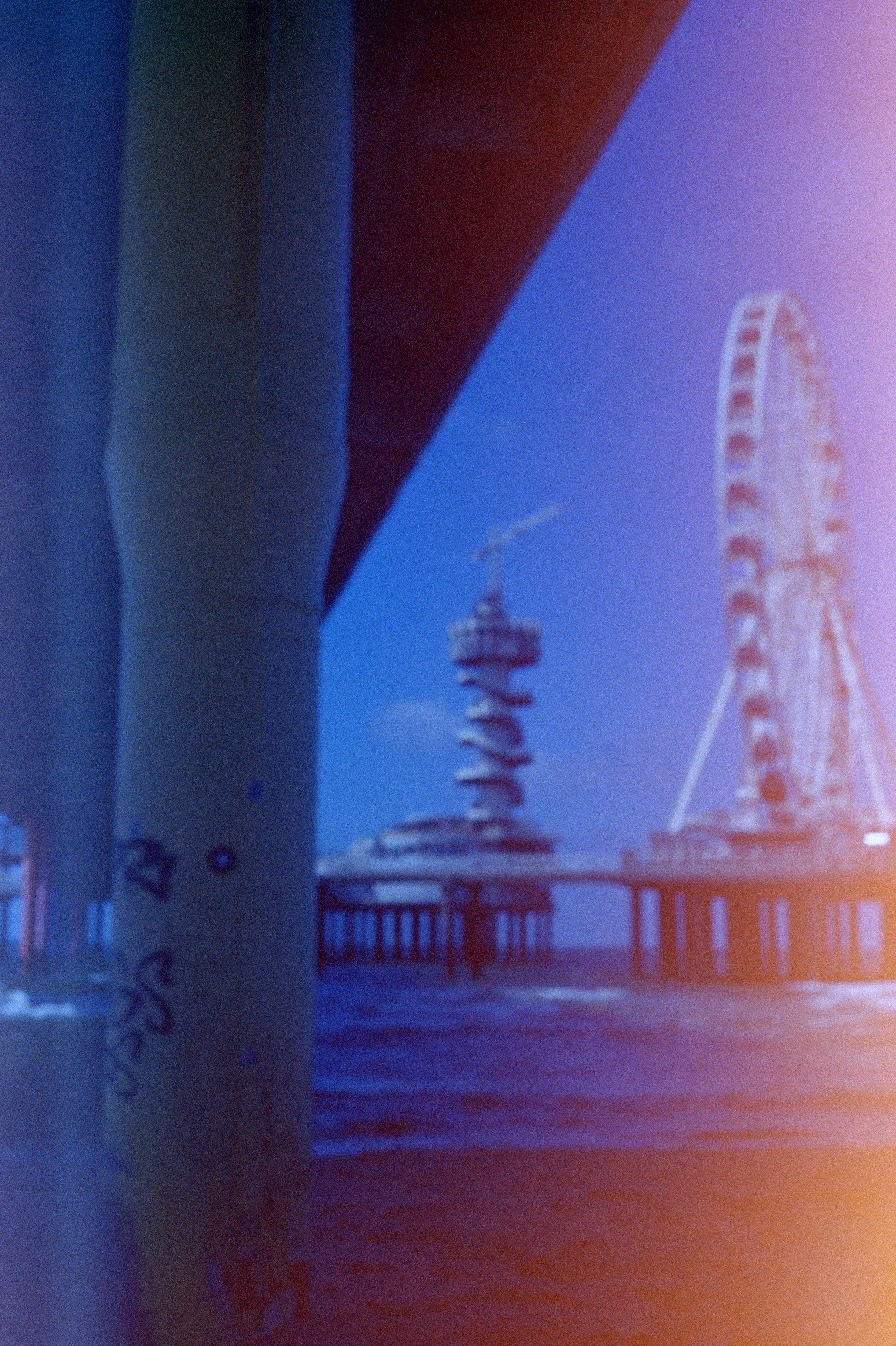 Blurry pier with ferris wheel and tower over water.