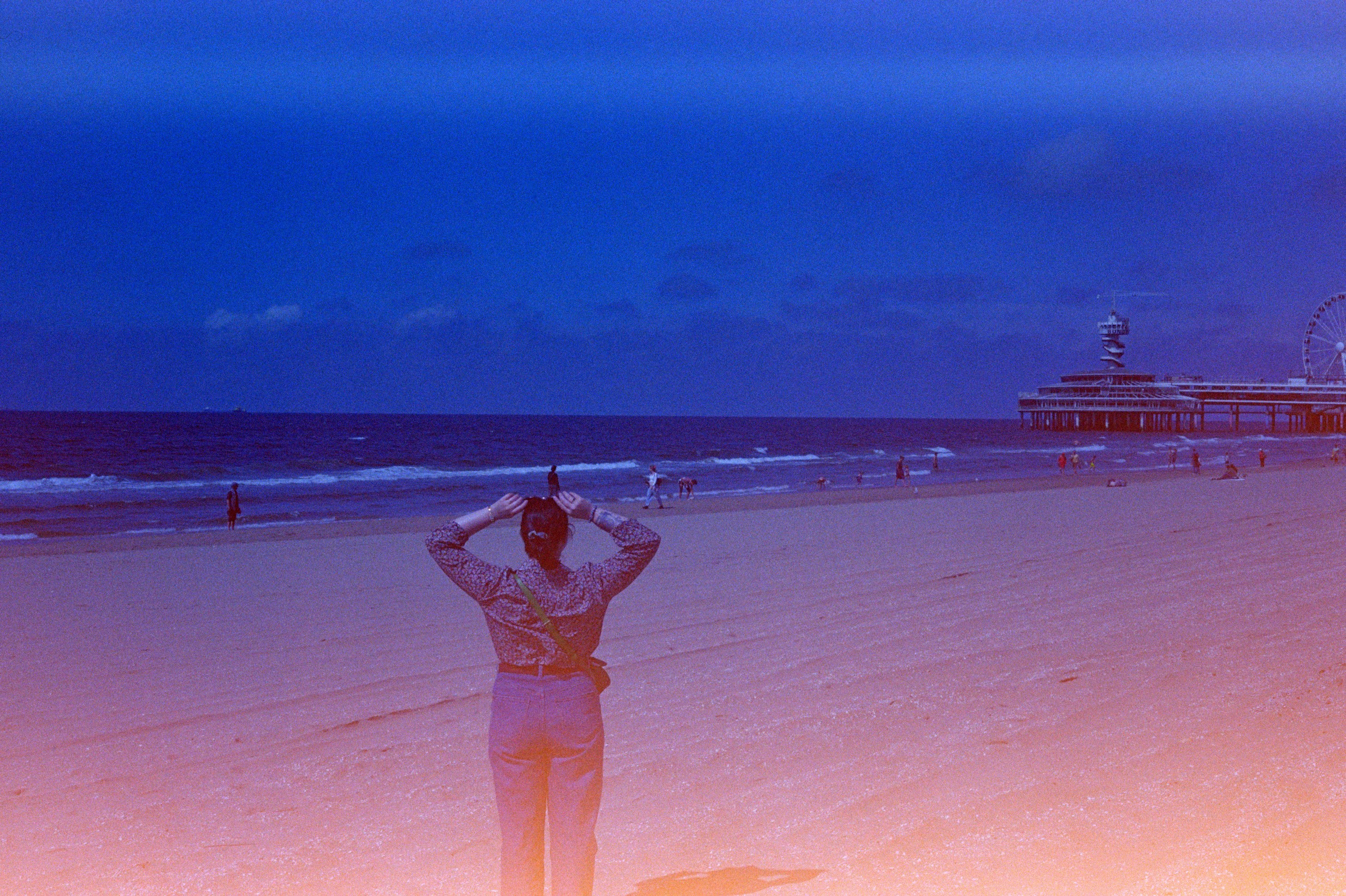 Person on beach looking at ocean and pier at dusk.