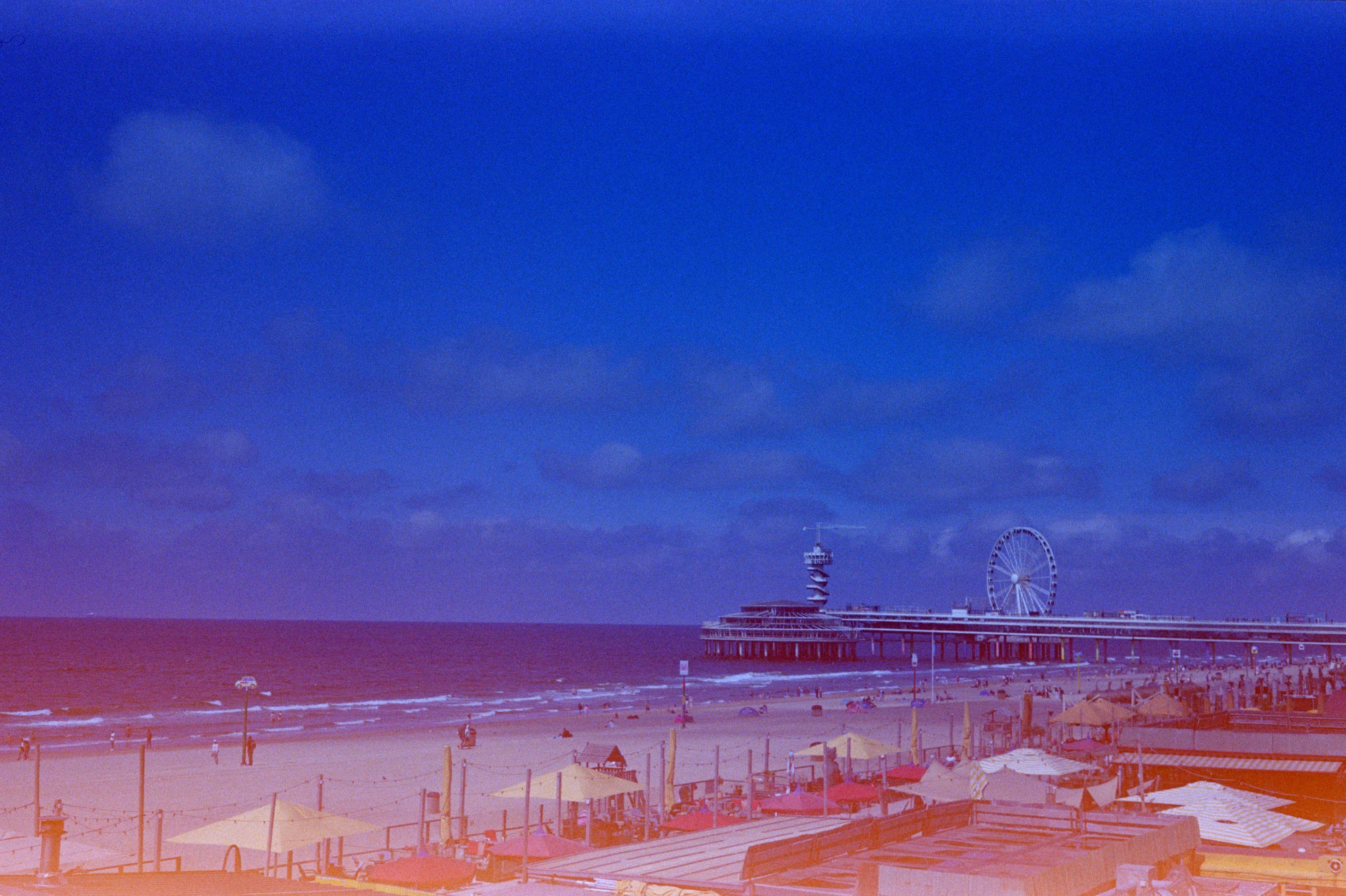 Pier, beach, and ocean under a vibrant blue sky.