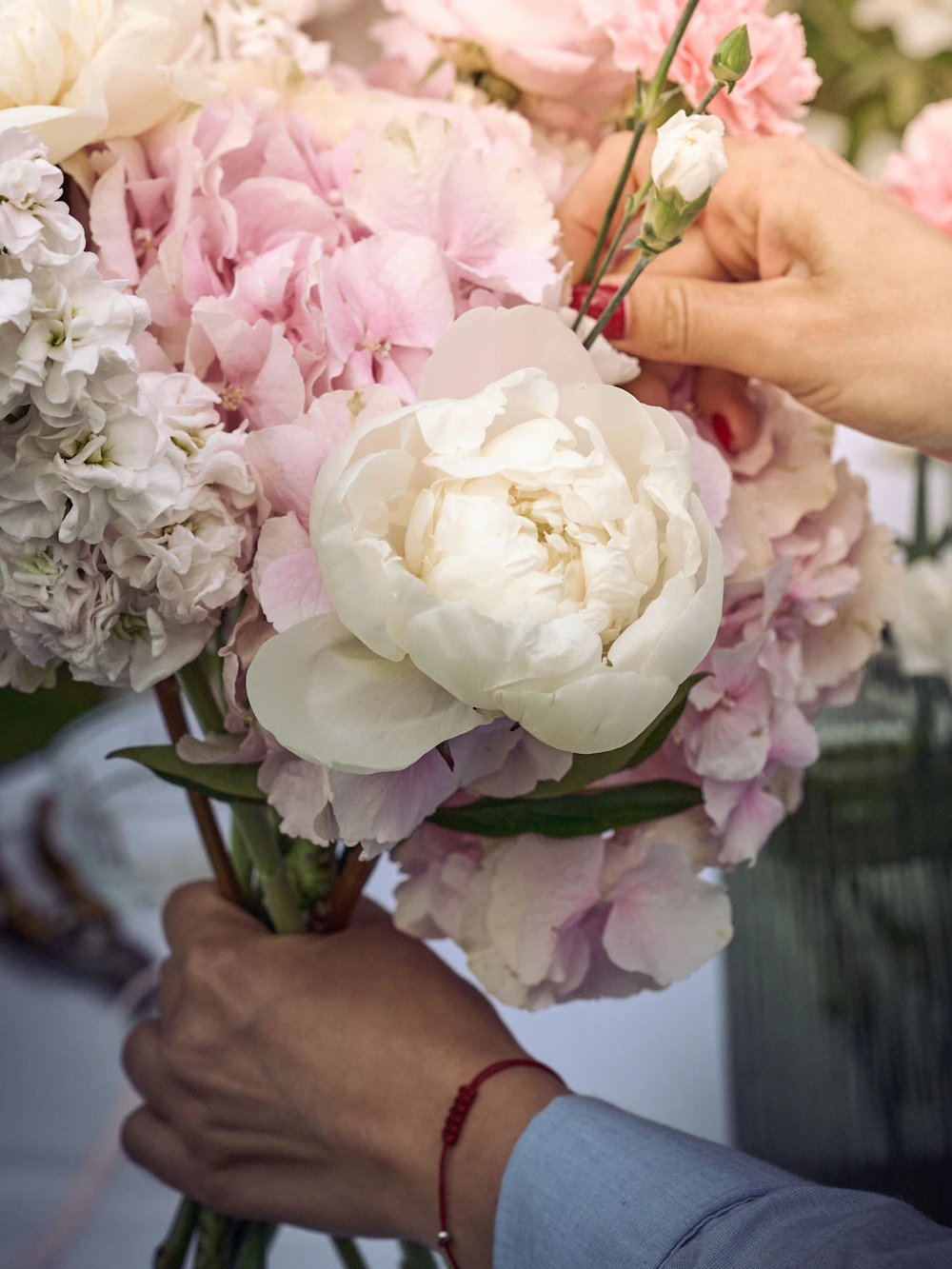 A florist's hands arranging a bouquet of pink and white peonies on the studio bench