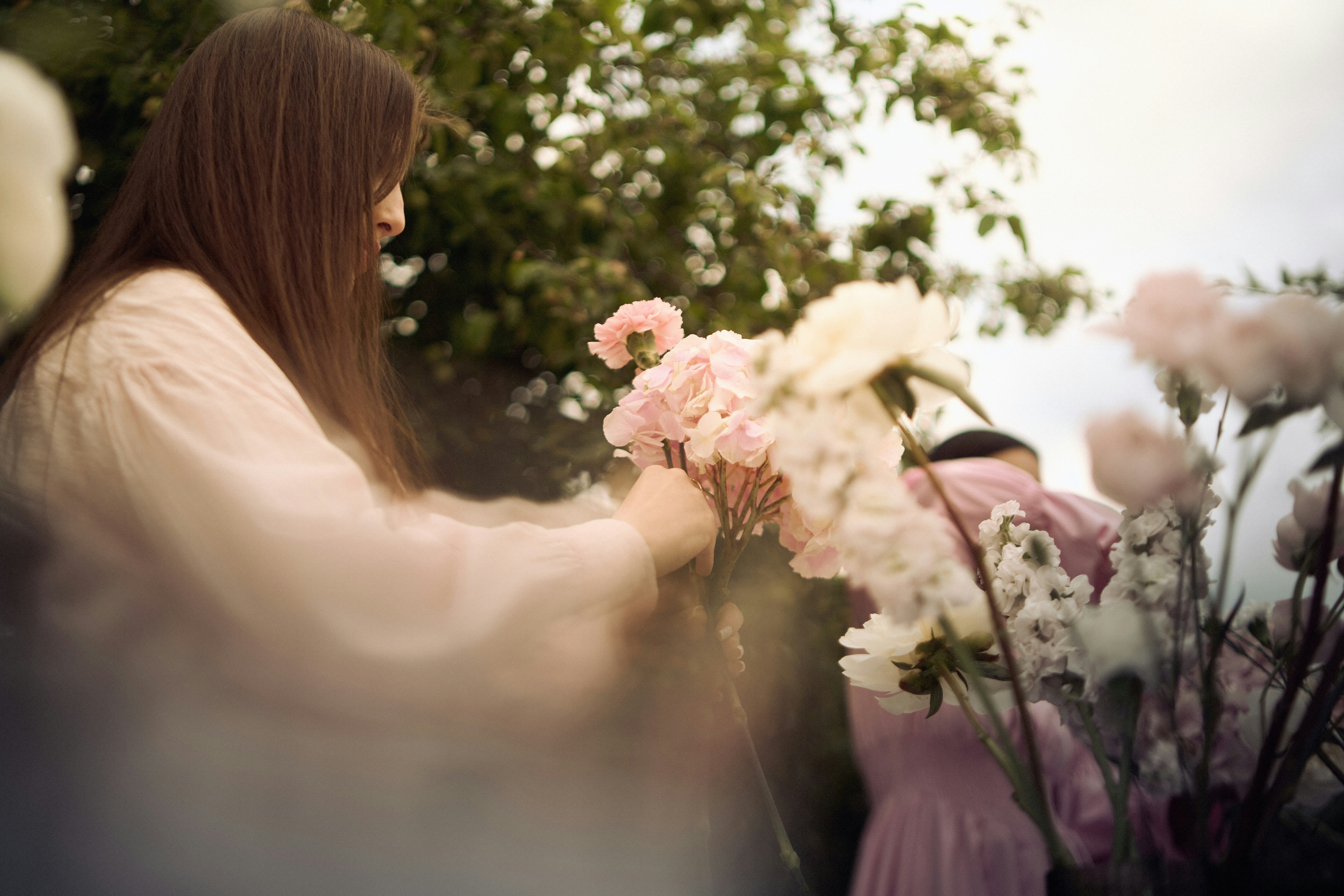 A florist's hands arranging pale peonies in soft morning light
