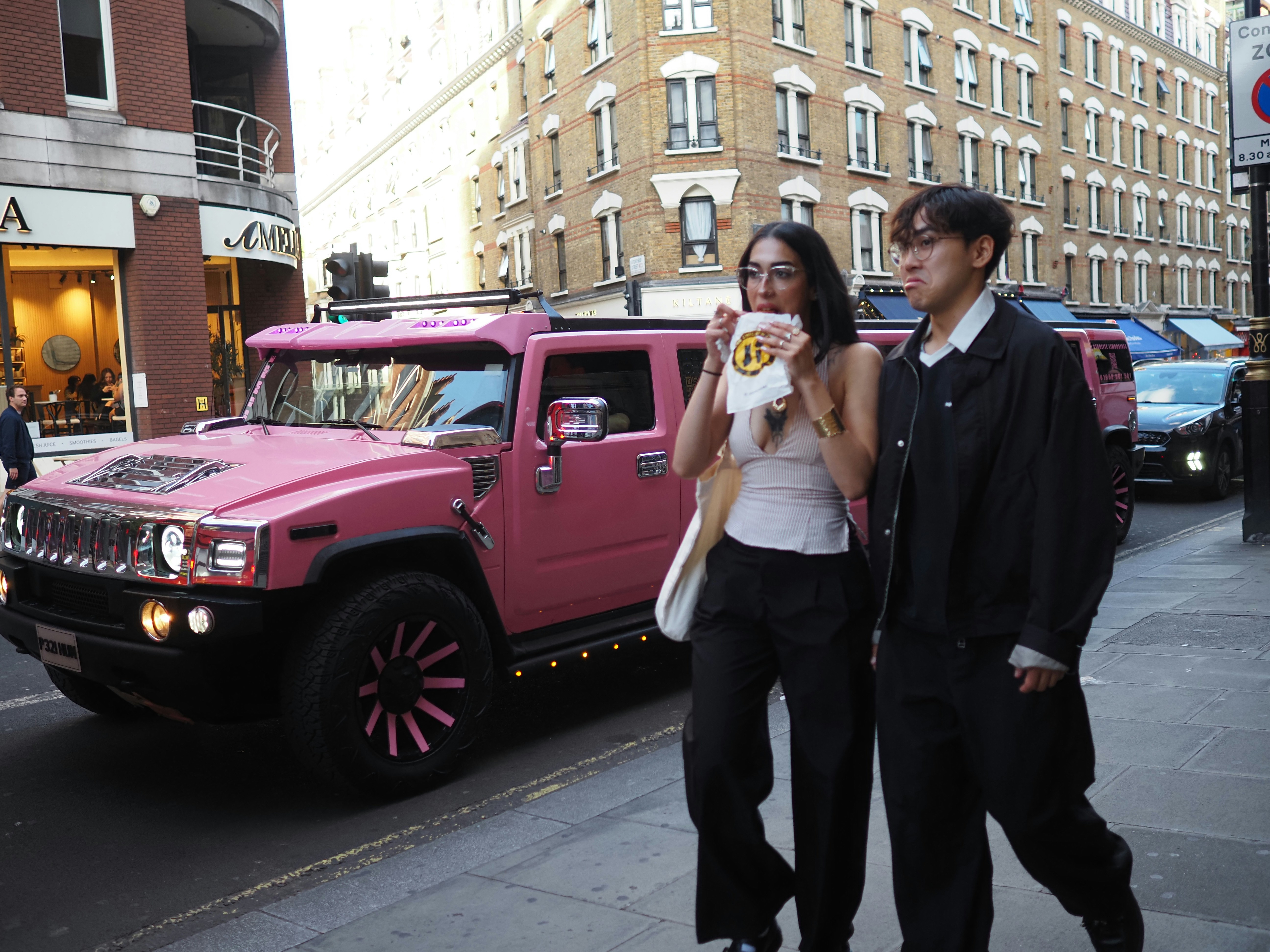 Woman eats popcorn while walking past a pink hummer.
