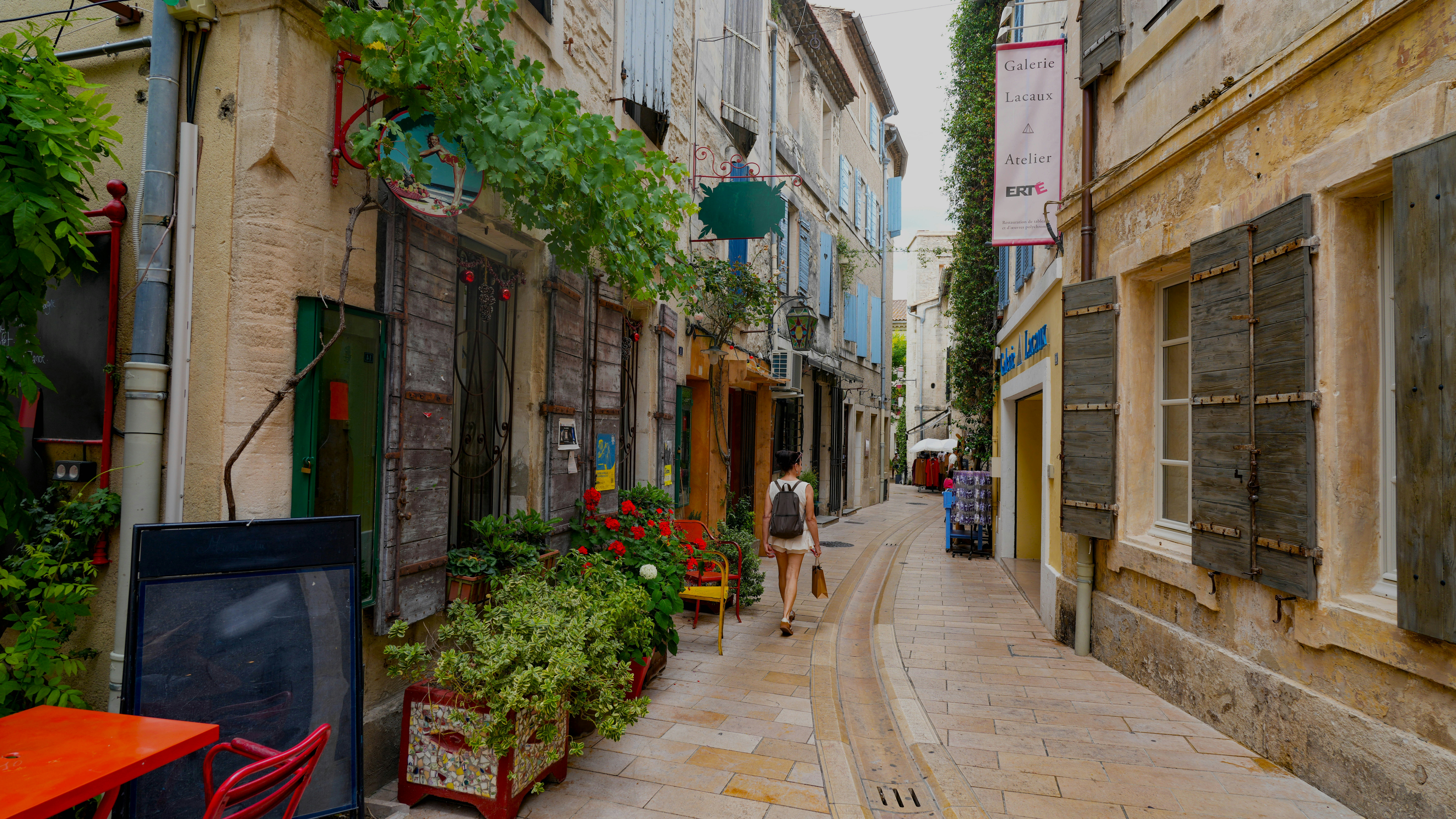 Narrow street with old buildings, plants, and a person walking.