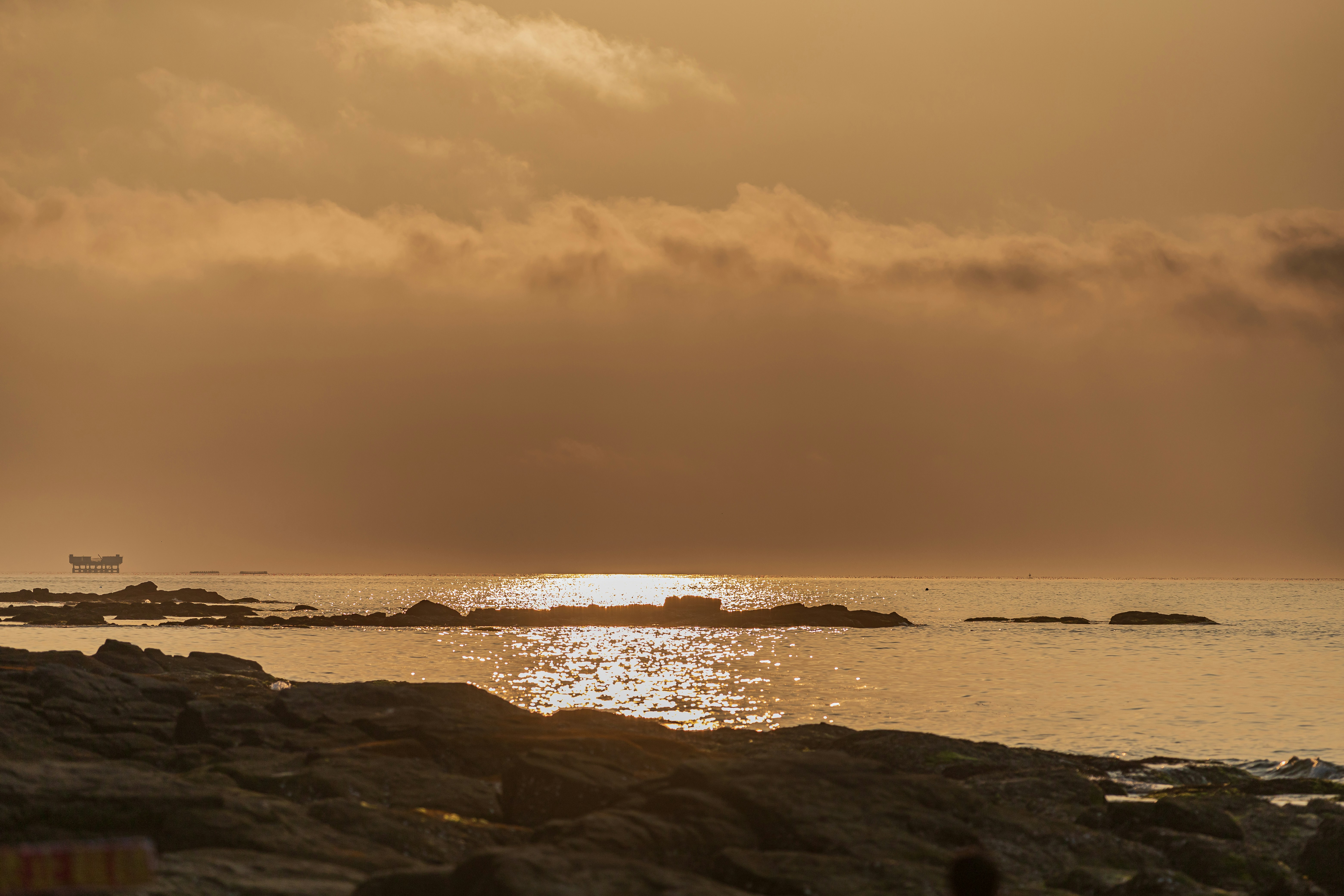 Golden sunset over a rocky ocean with shimmering water.