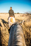 A person rides a horse through dry, golden grass.