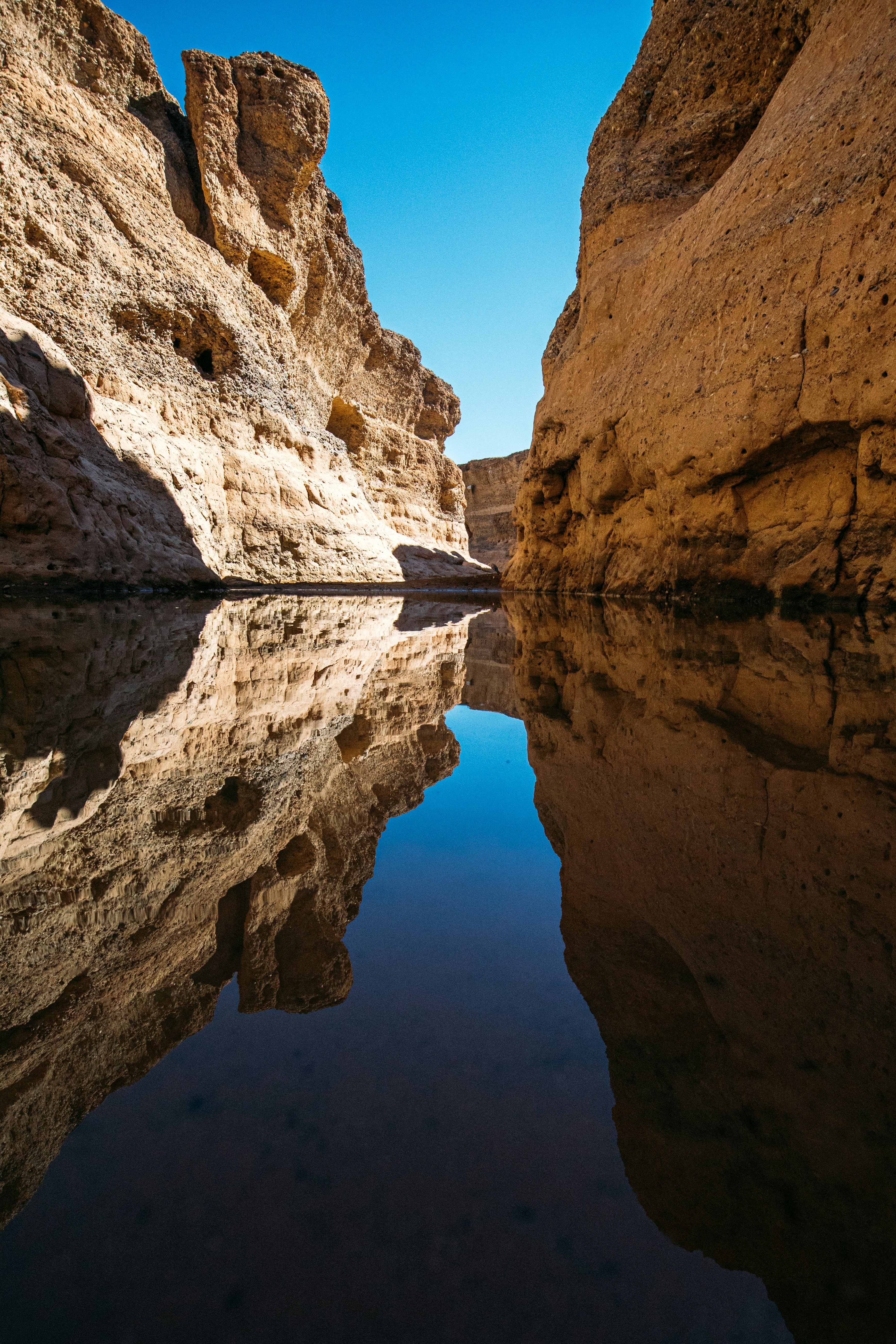Narrow desert canyon with water reflections under a blue sky.