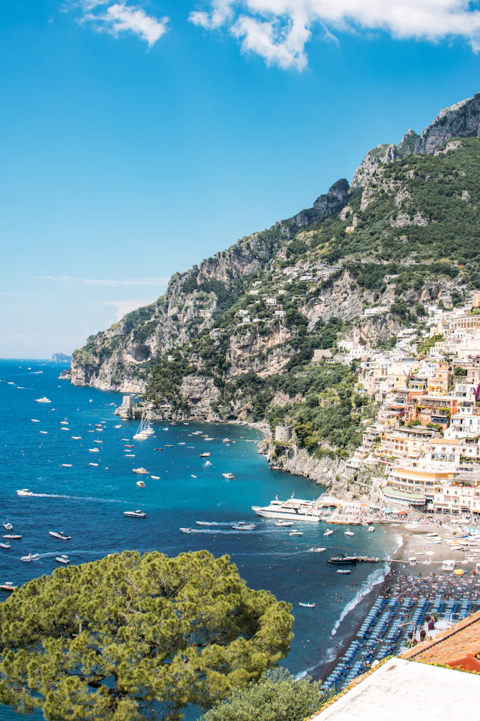 A pastel coastal town stacked above a beach lined with umbrellas.