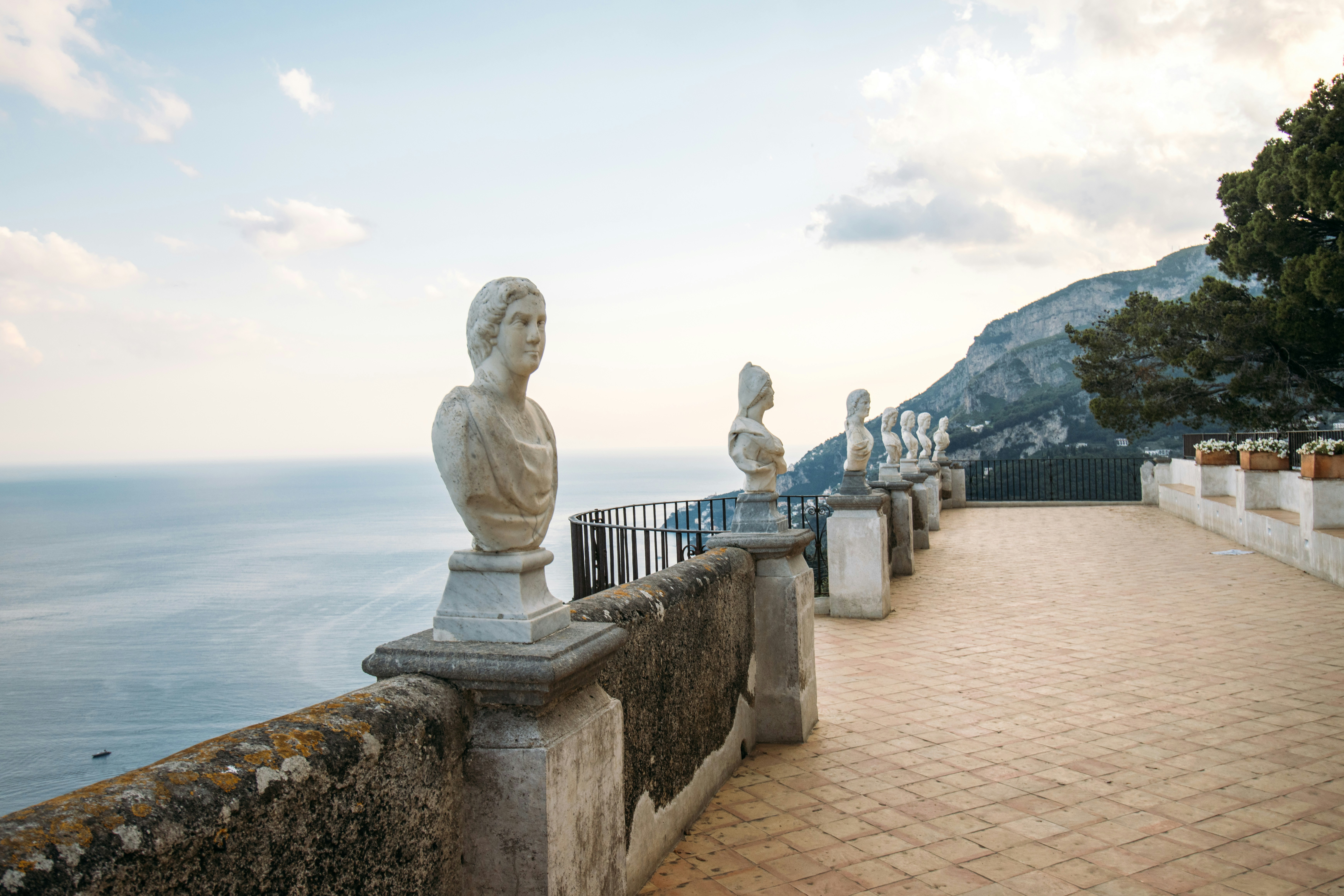 Stone busts line a balcony overlooking the sea and mountains