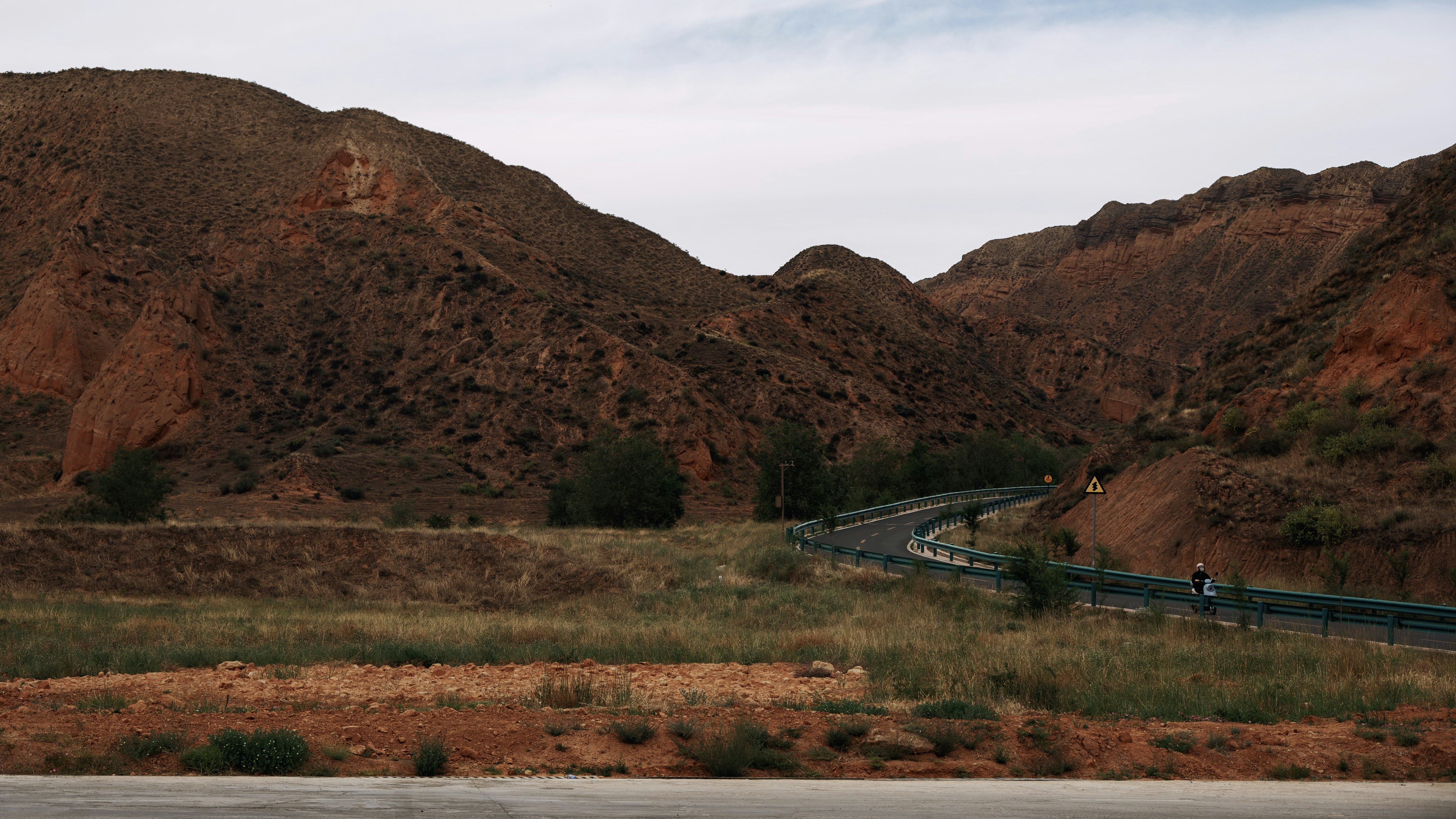 A winding road cuts through reddish-brown mountains and green fields.