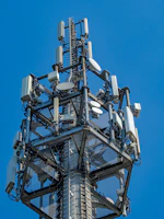 A tall telecommunications tower with many antennas against blue sky.