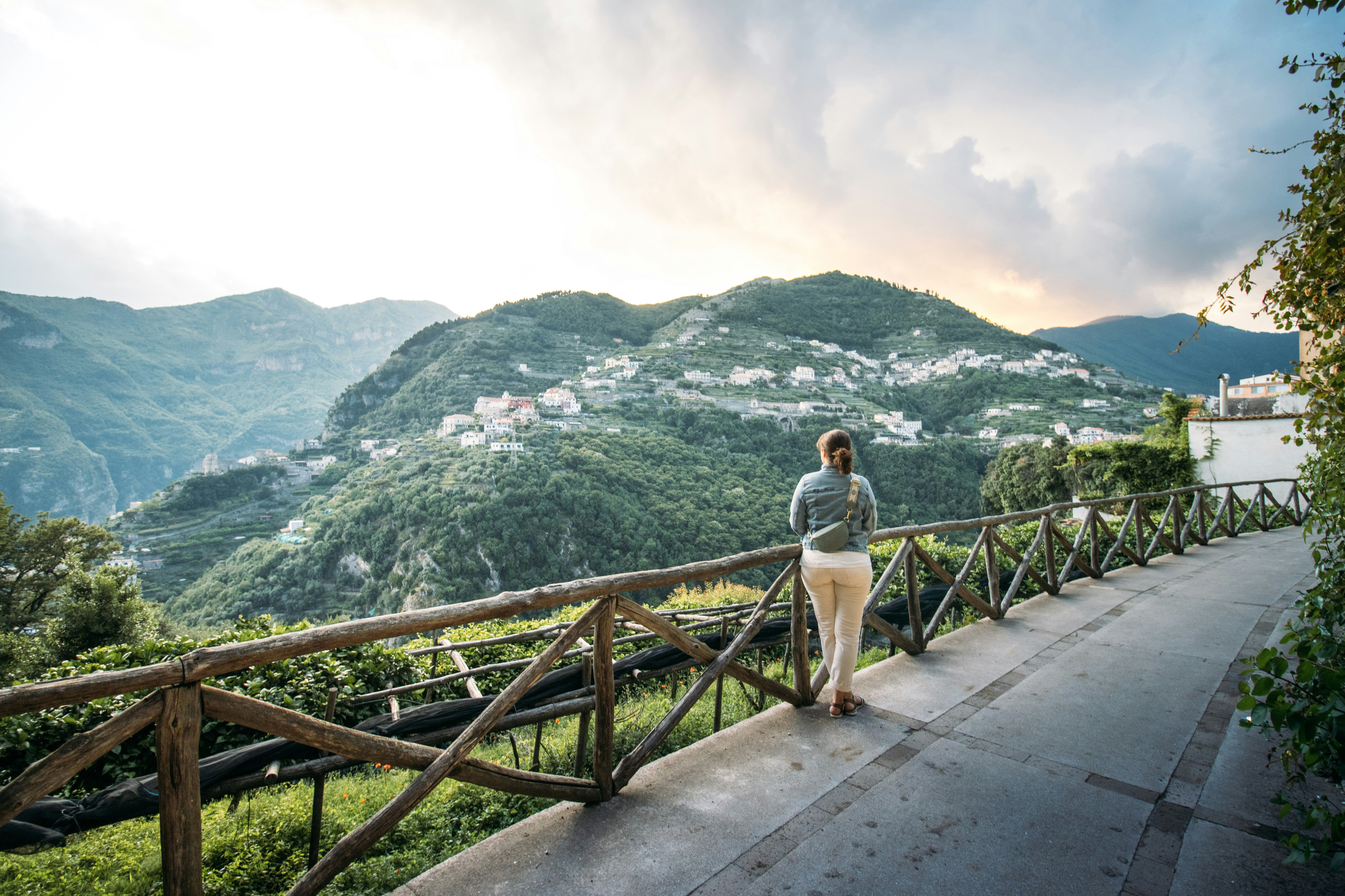 A woman stands on a path overlooking a mountainous village.