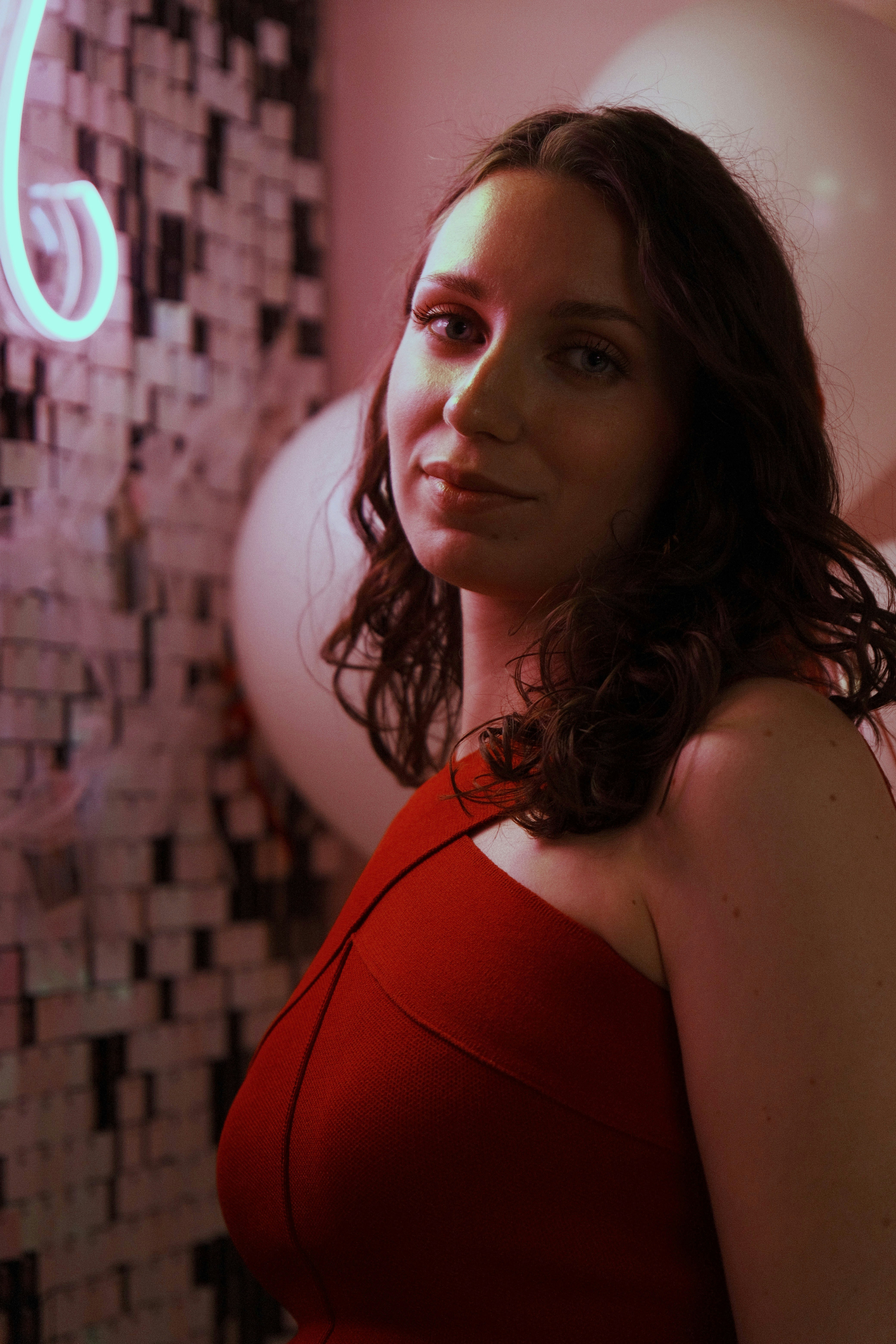 Woman in red dress with pink neon light and balloons.