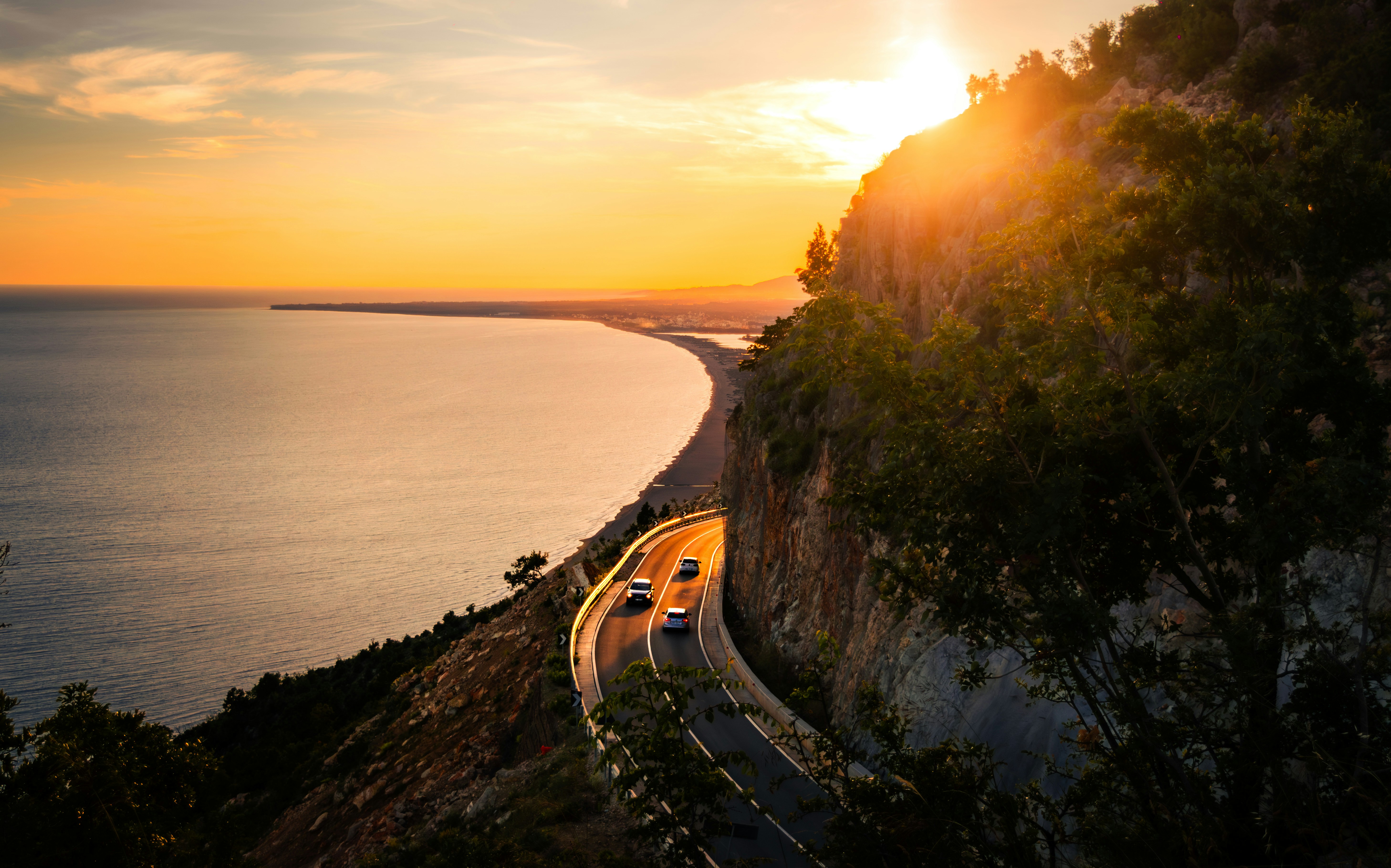 Golden sunset illuminates a winding coastal road and ocean.