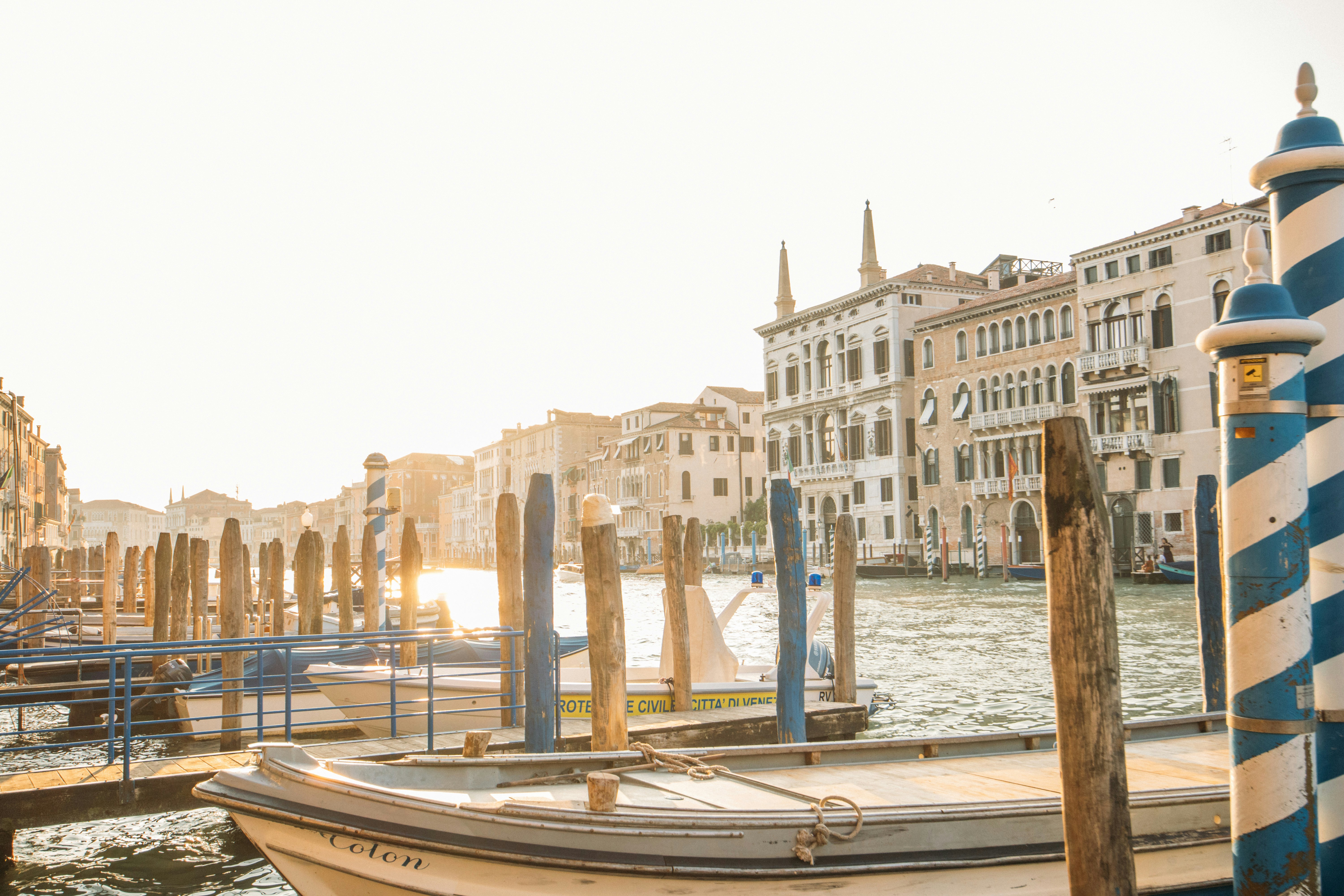 Boats docked in a sunny venetian canal with historic buildings.