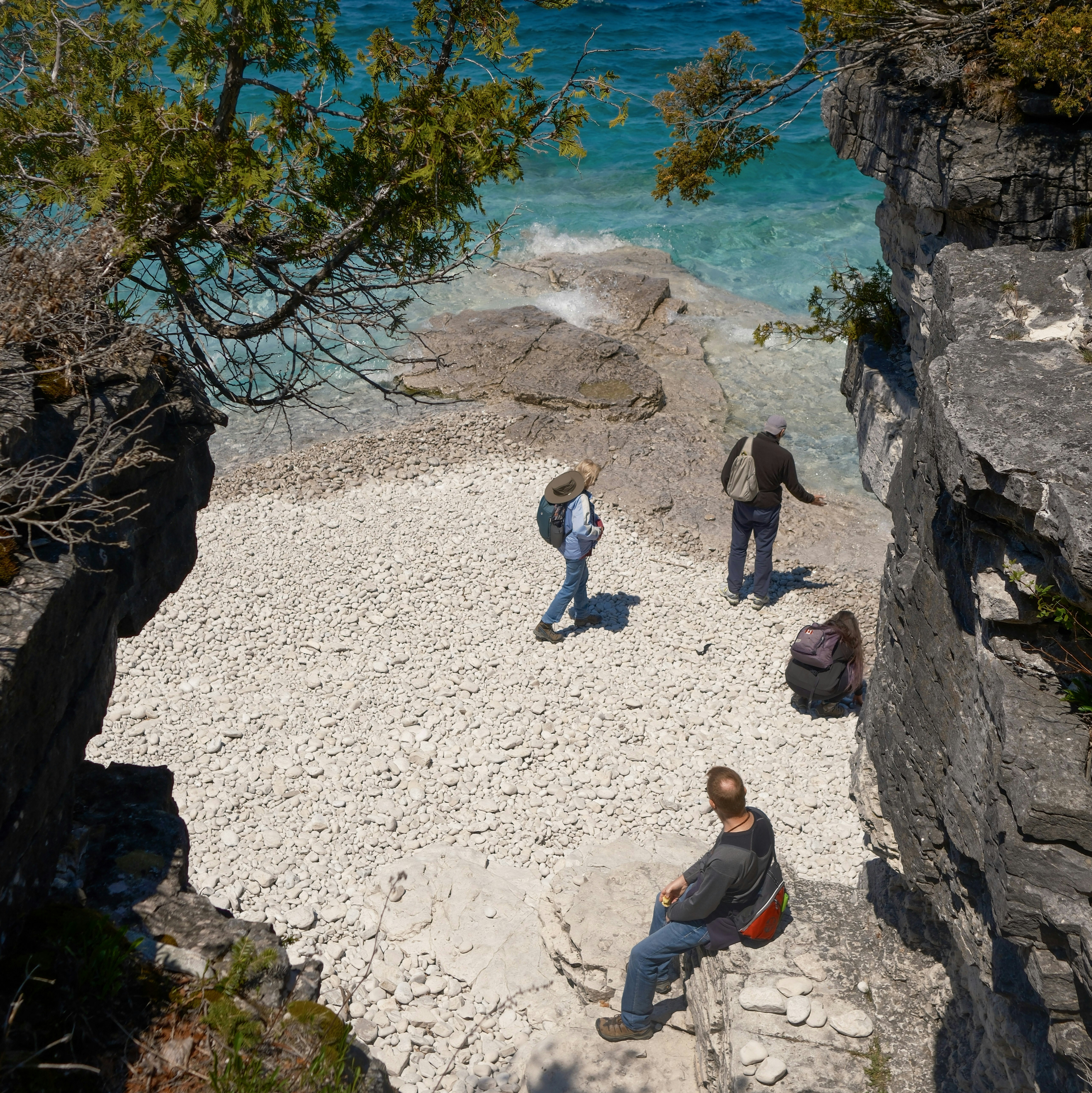 Three people exploring a rocky beach with turquoise water.