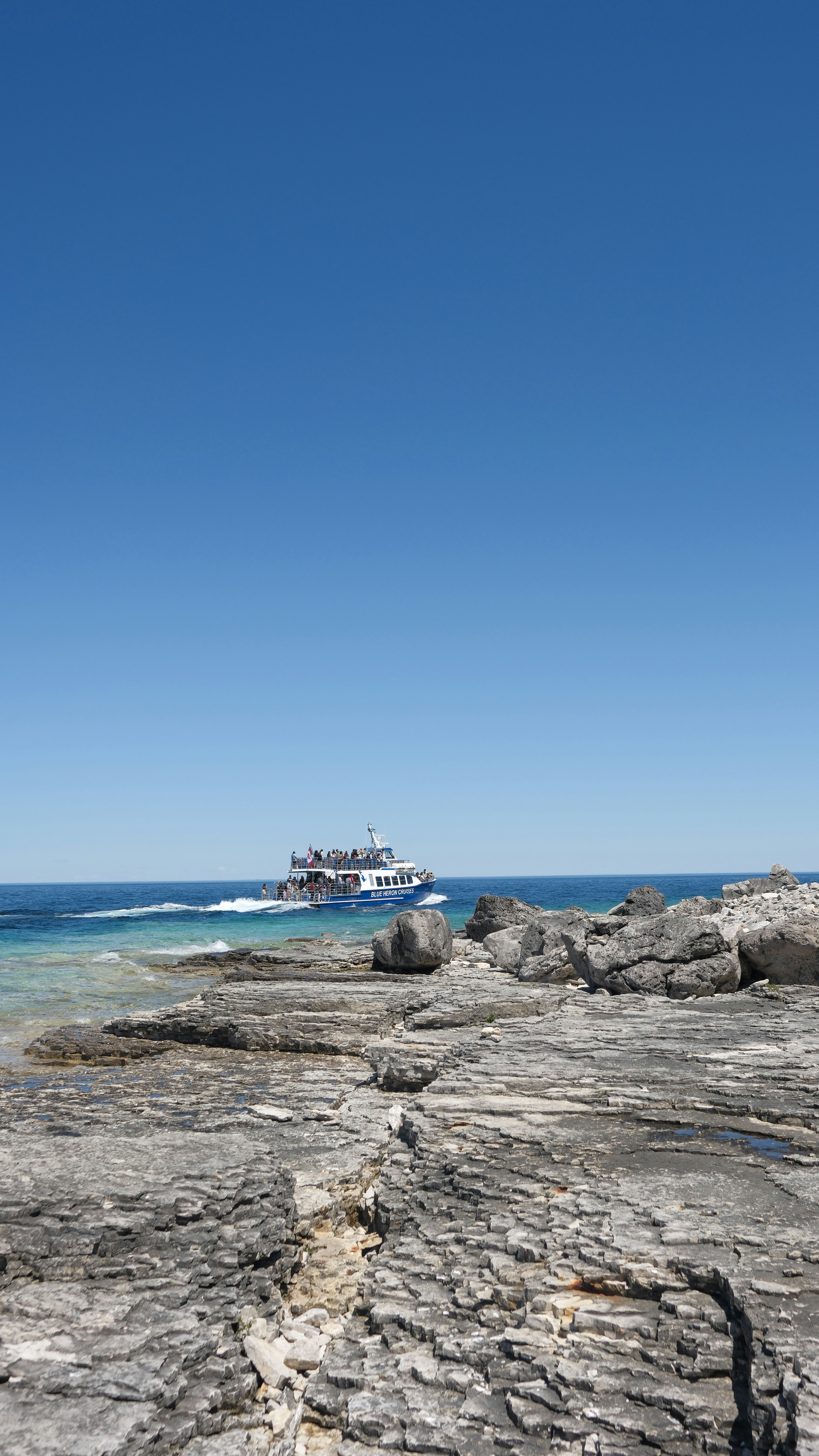 Boat sailing past rocky shore on vibrant blue water.