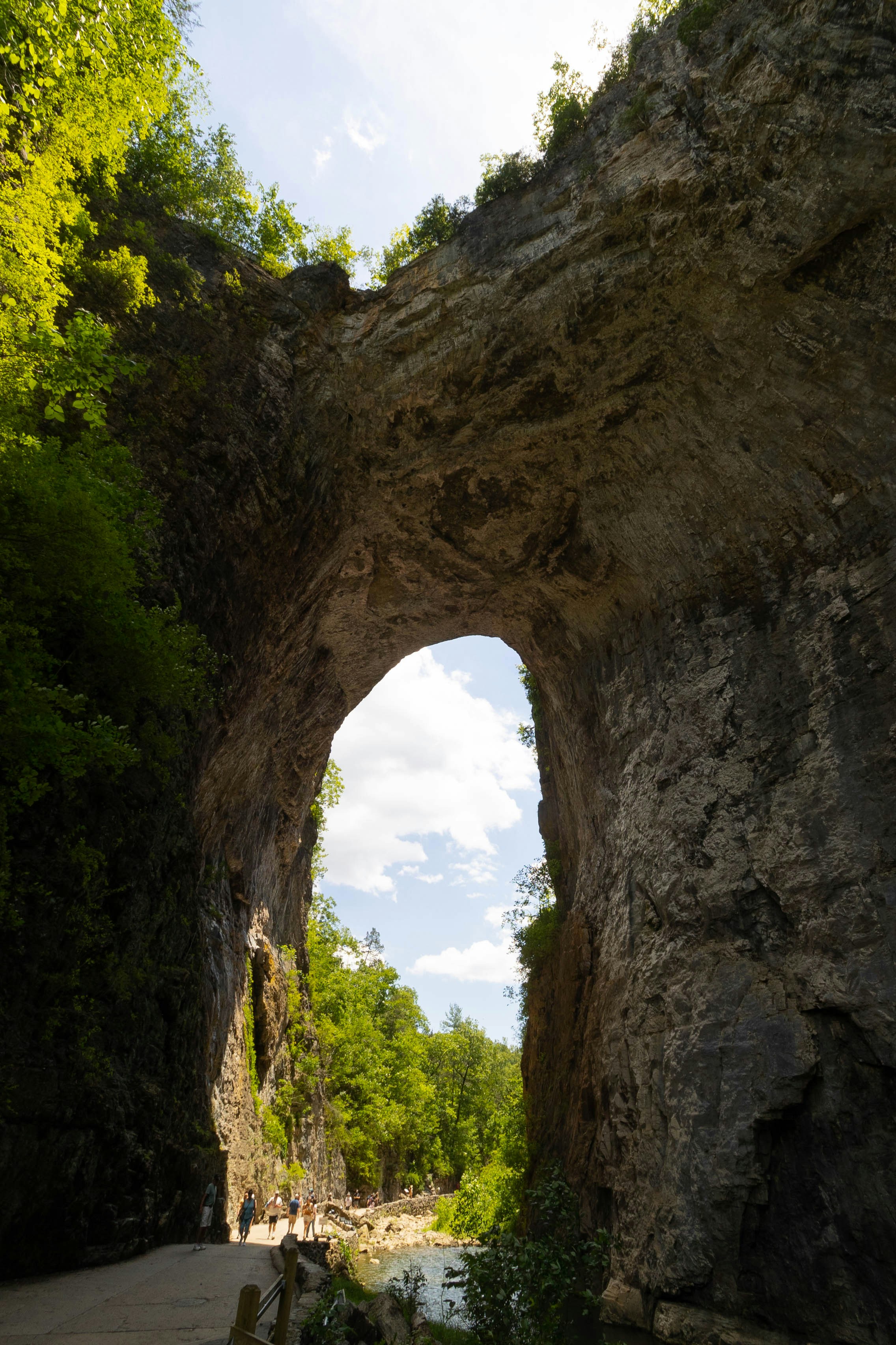 Um enorme arco rochoso natural emoldura uma paisagem ensolarada e verde.