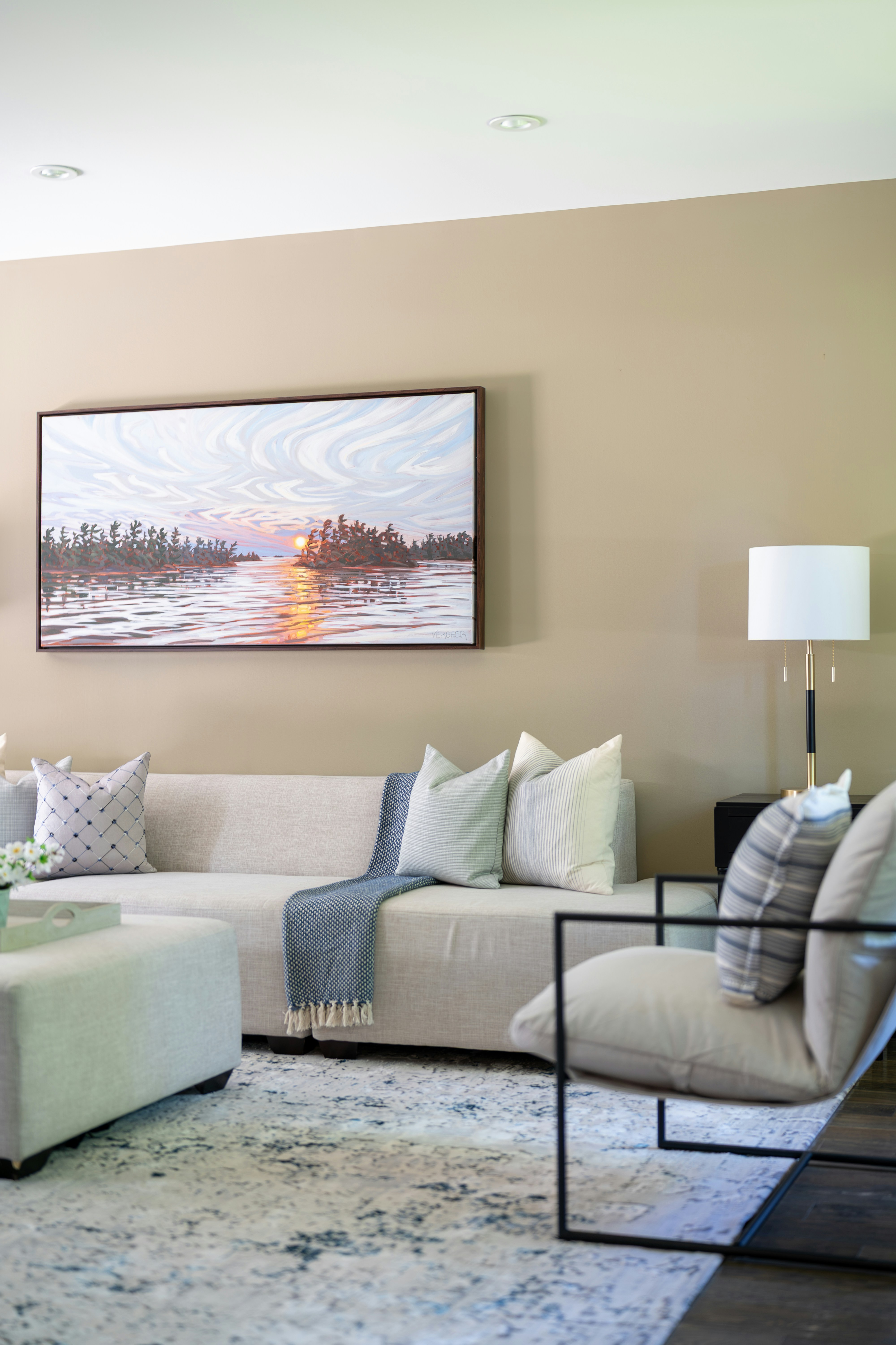 Elegant living room with a sofa, armchair, and sunset painting.