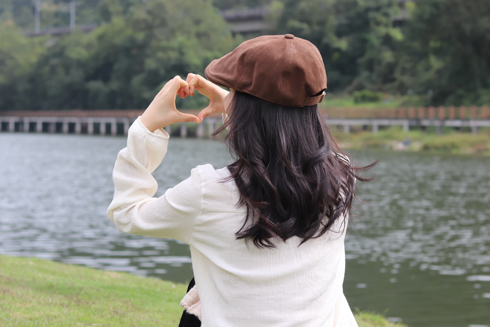Person making a heart shape with hands by a lake