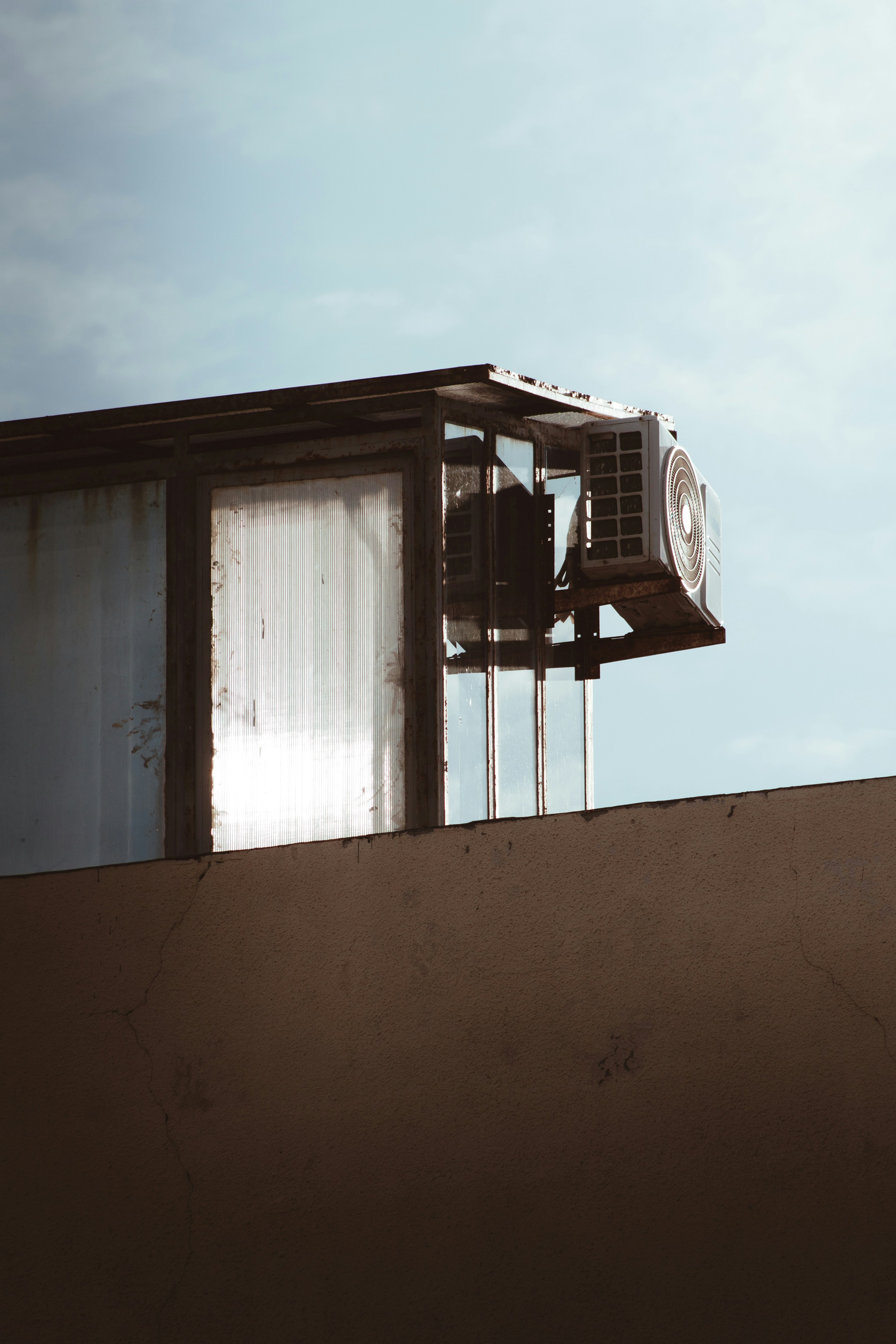 An old air-conditioning unit on a frame at the edge of a building rooftop