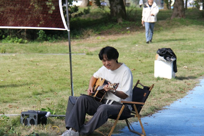 A musician playing acoustic guitar outdoors in a park setting at dusk