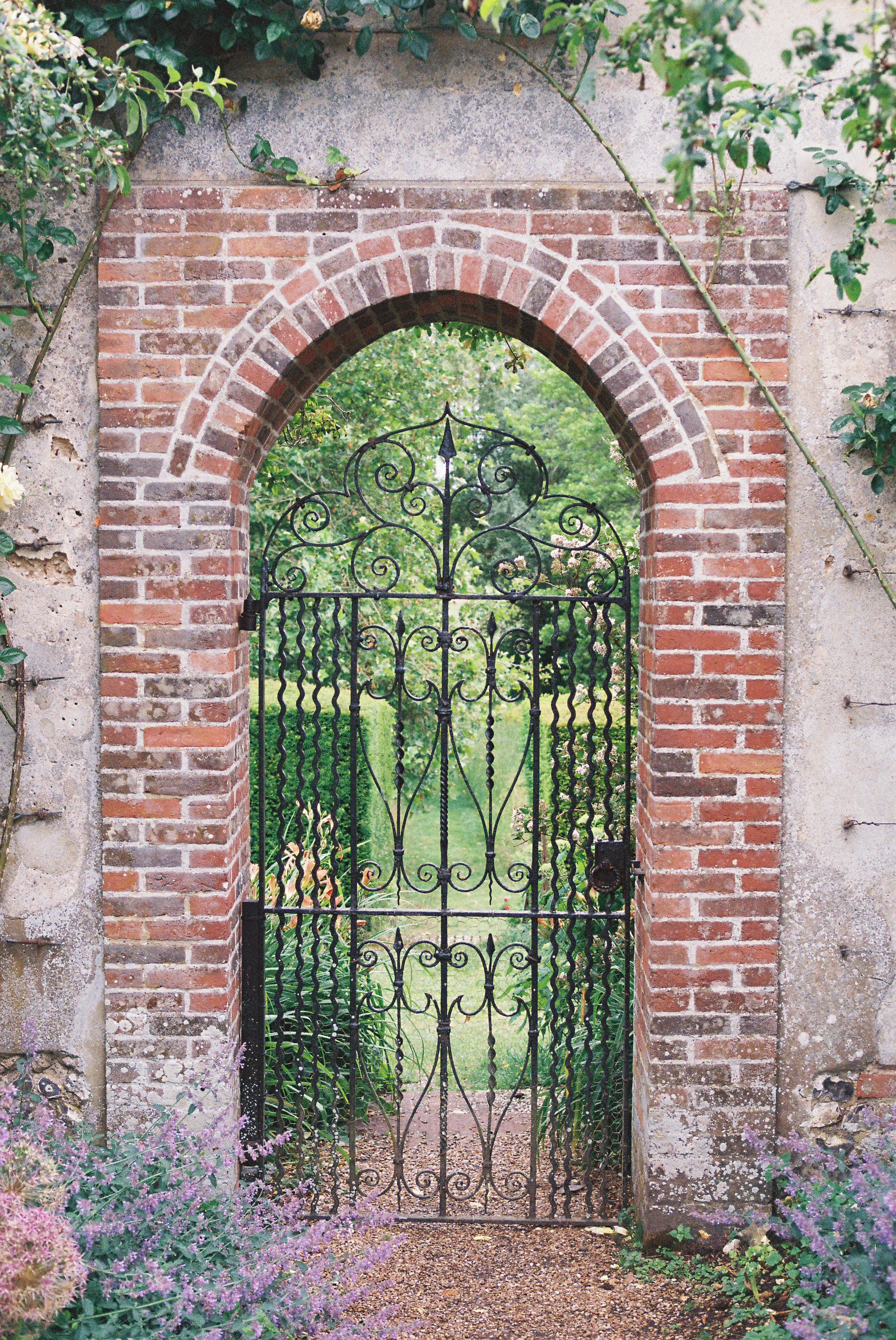 Cancello metallico ornato in un arco in mattoni verso il giardino