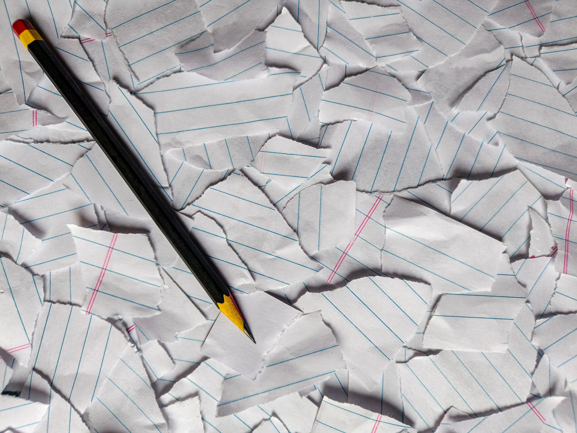 A pencil on a pile of torn, crumpled lined paper.