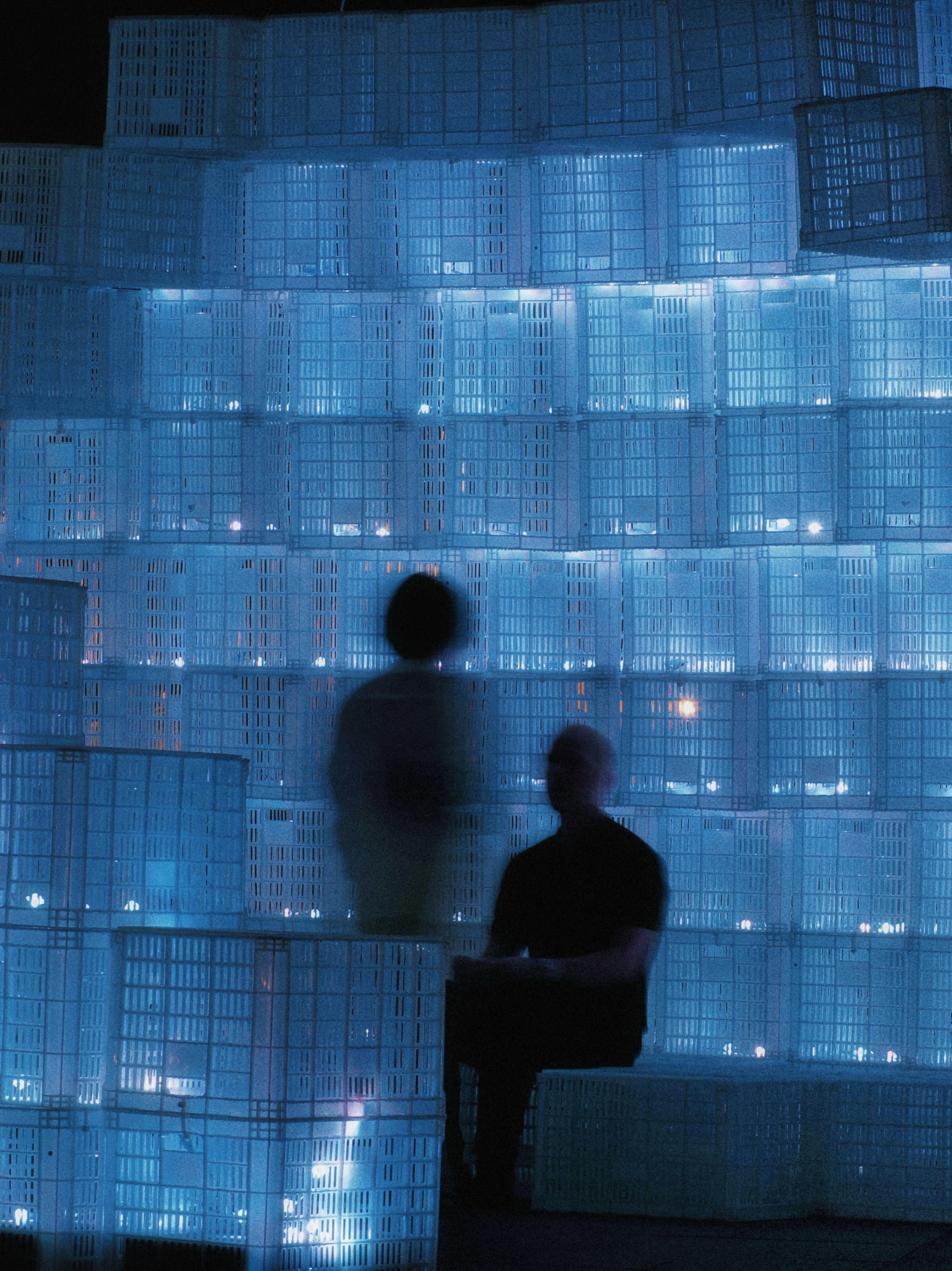 Two figures sit by a glowing blue crate wall.