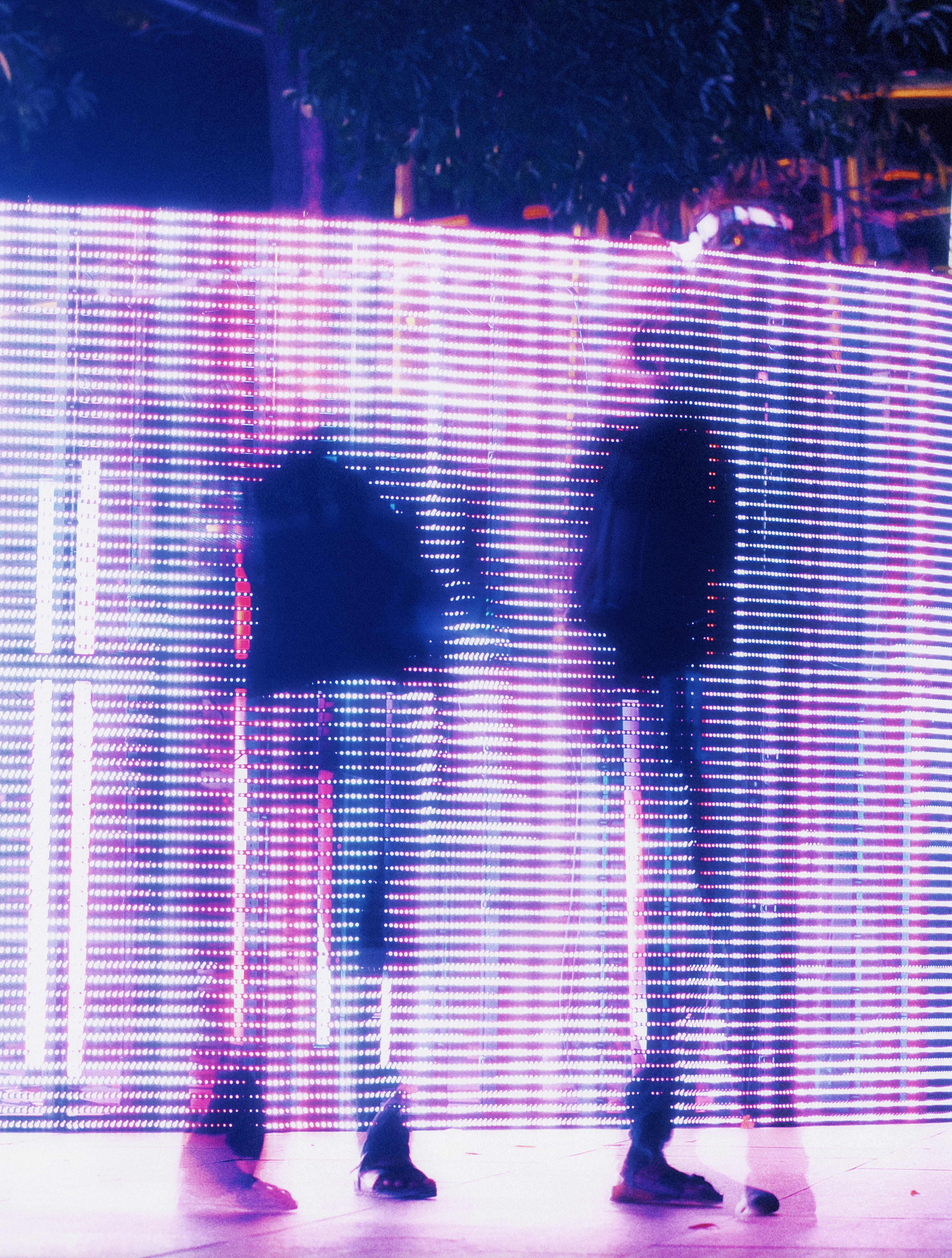 Two blurred figures walking past a glowing purple light wall.