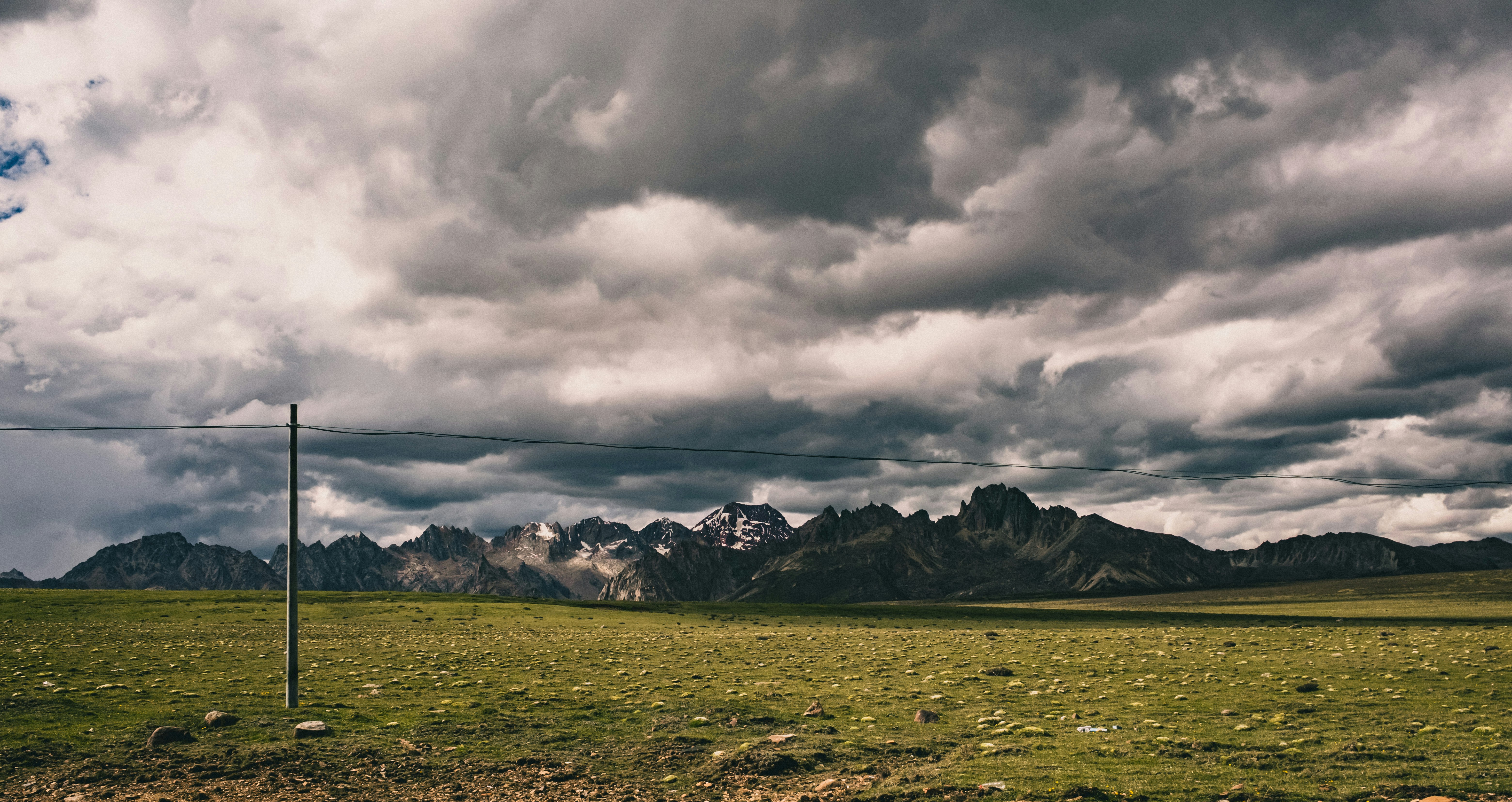 Green field and mountains under a dramatic, cloudy sky.