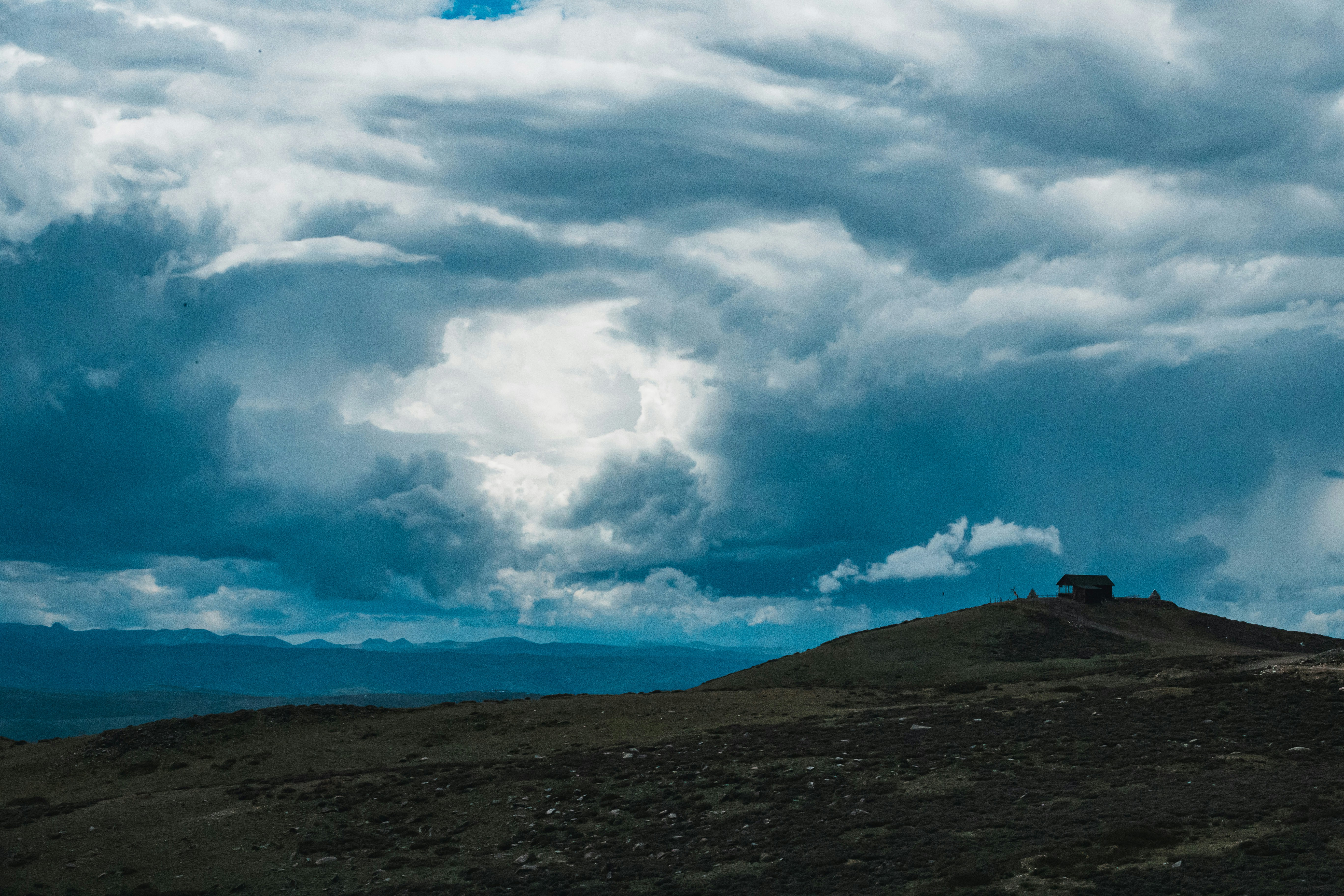 A small building on a hill under dramatic cloudy sky.
