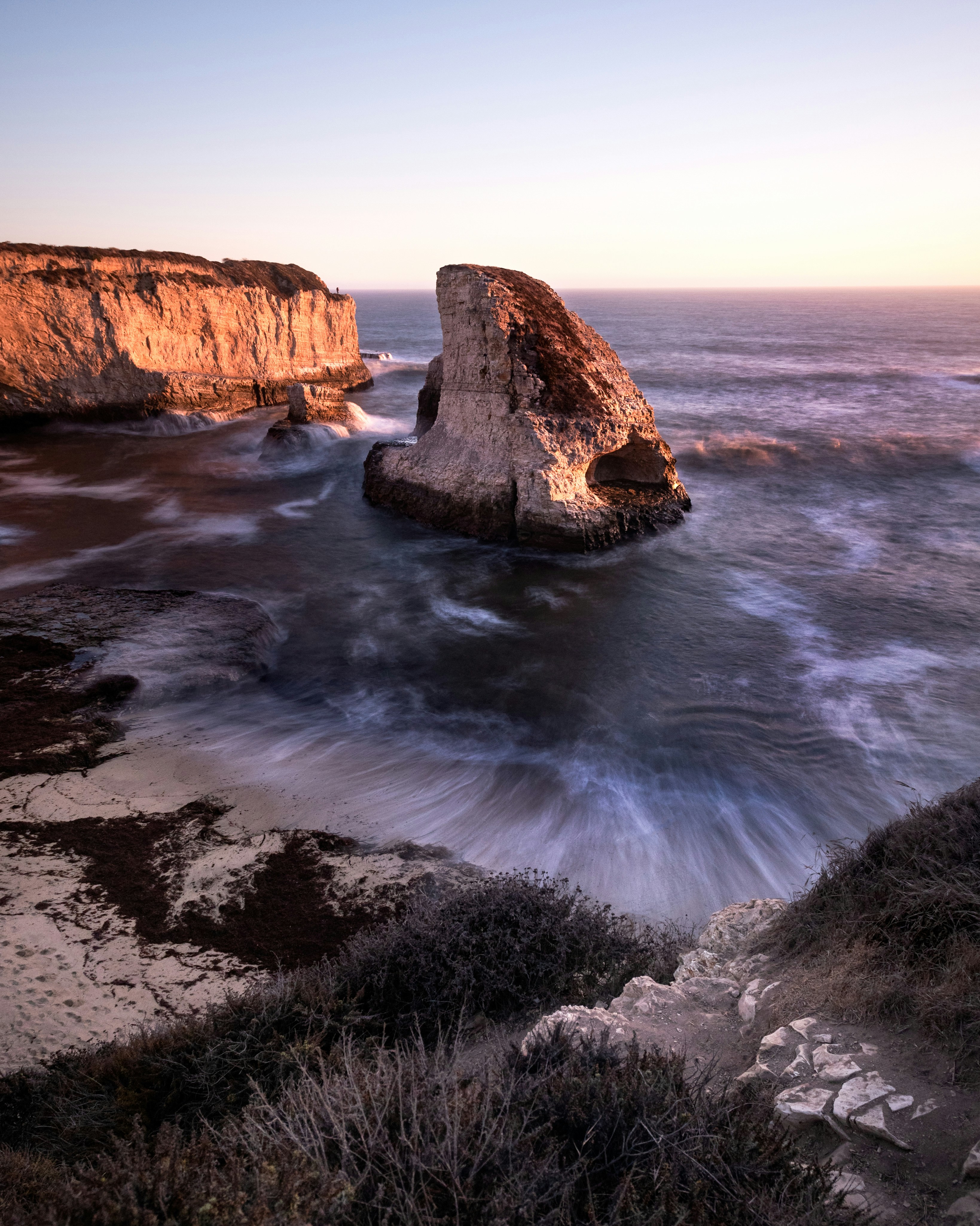 Dramatic sea stack and cliffs illuminated by golden hour light.