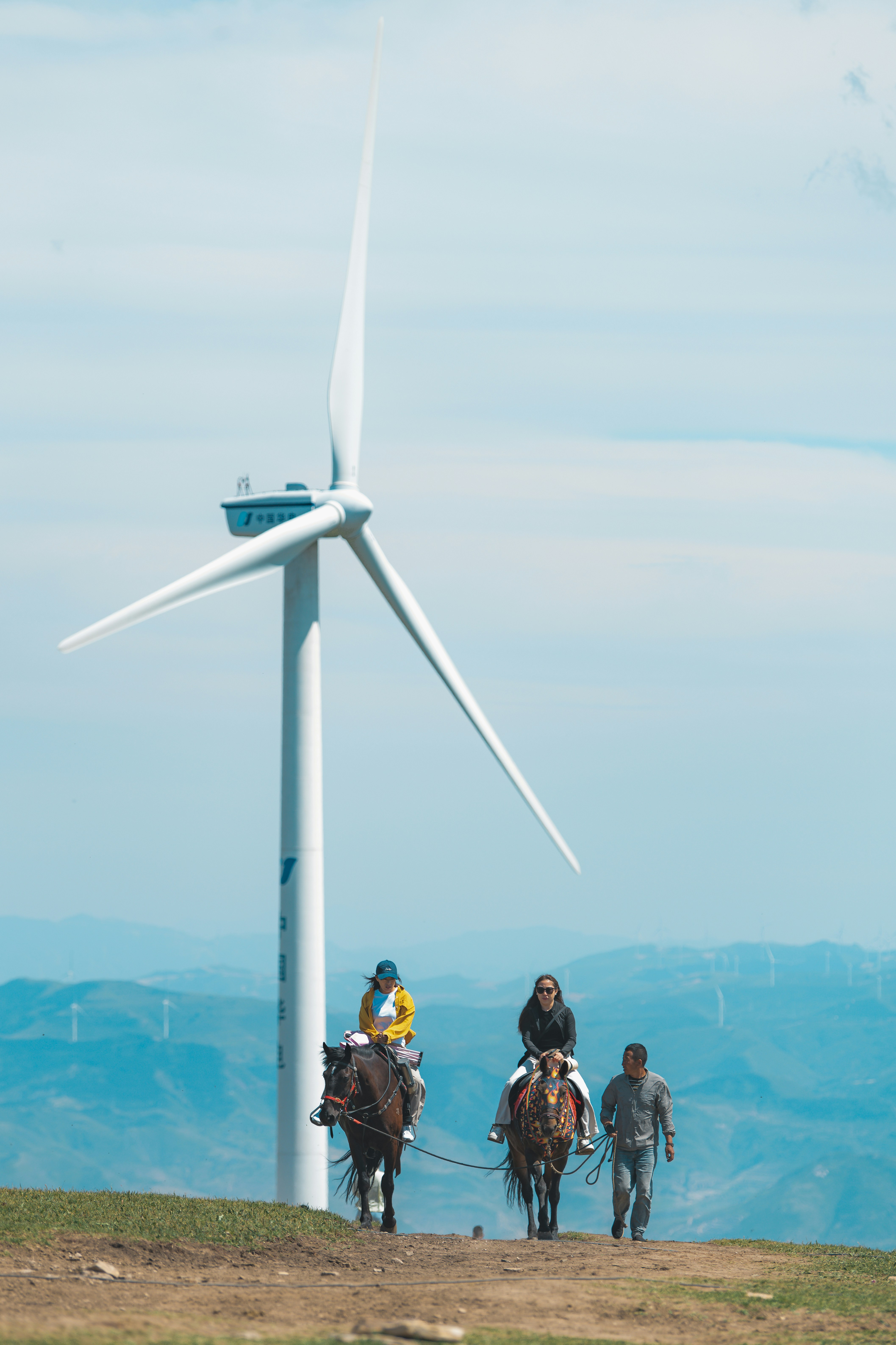 Deux cyclistes et un marcheur près d’une grande éolienne.