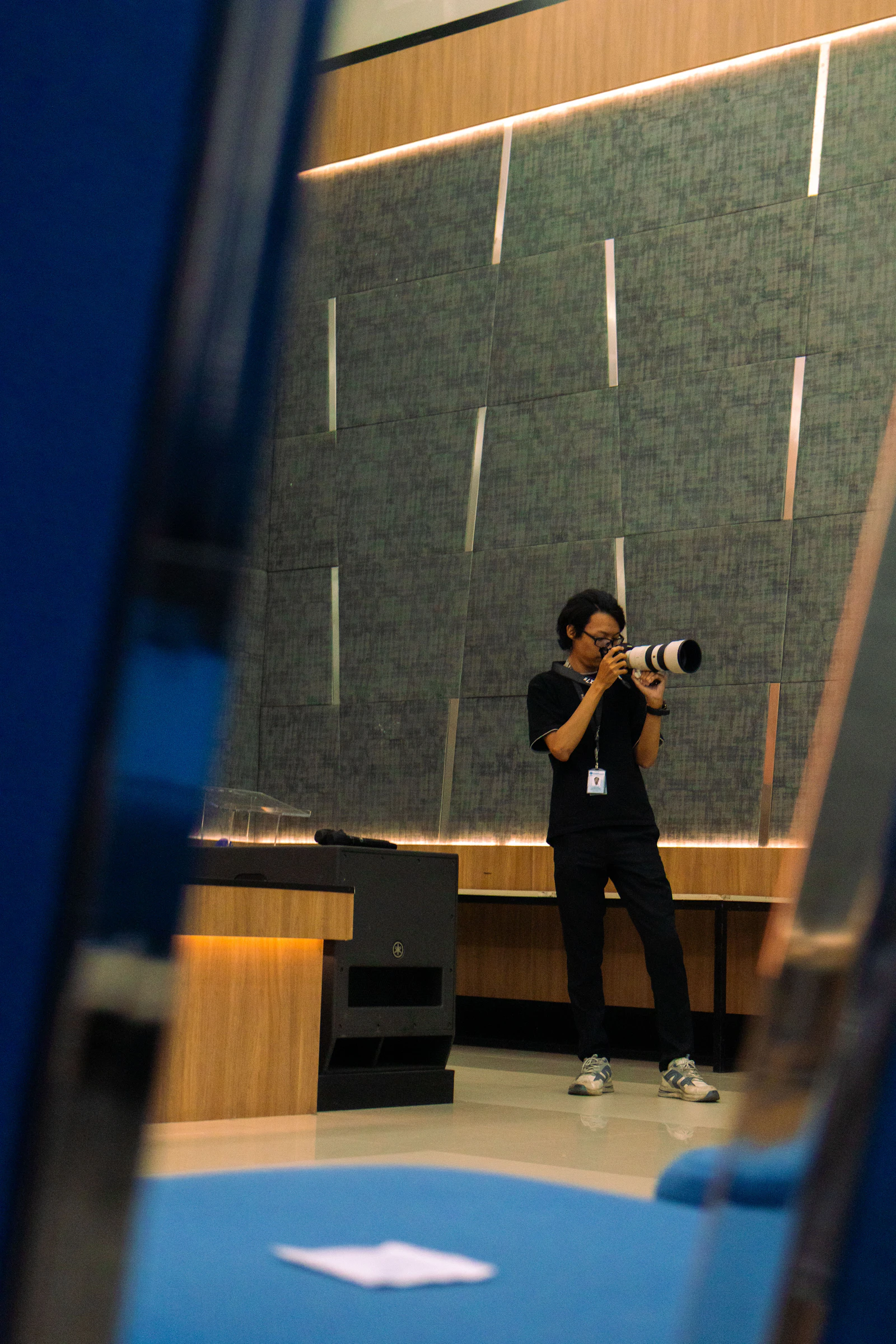 An event photographer with a telephoto lens in an auditorium, framed between rows of seats