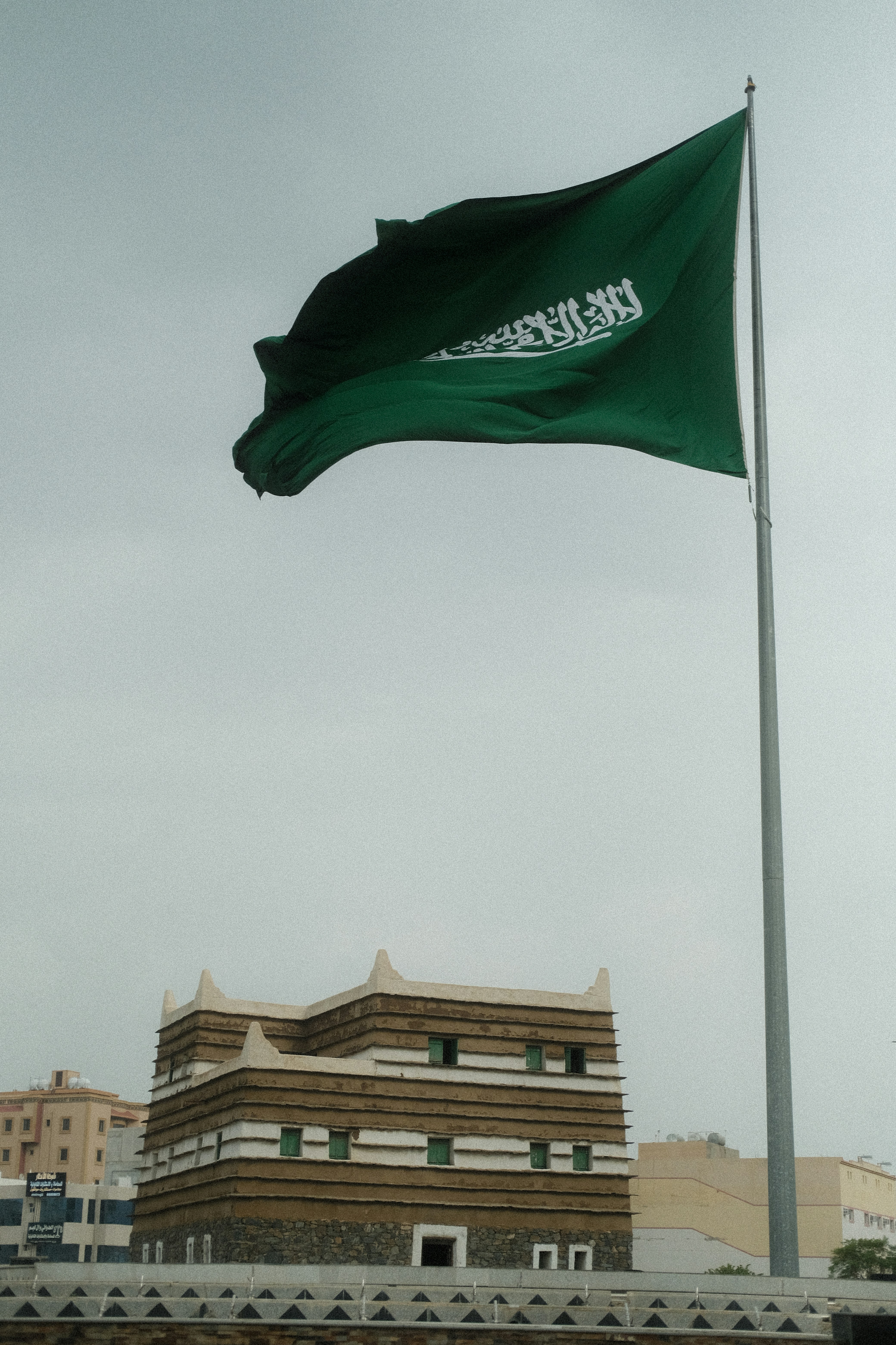 A saudi arabian flag waves above a traditional building.