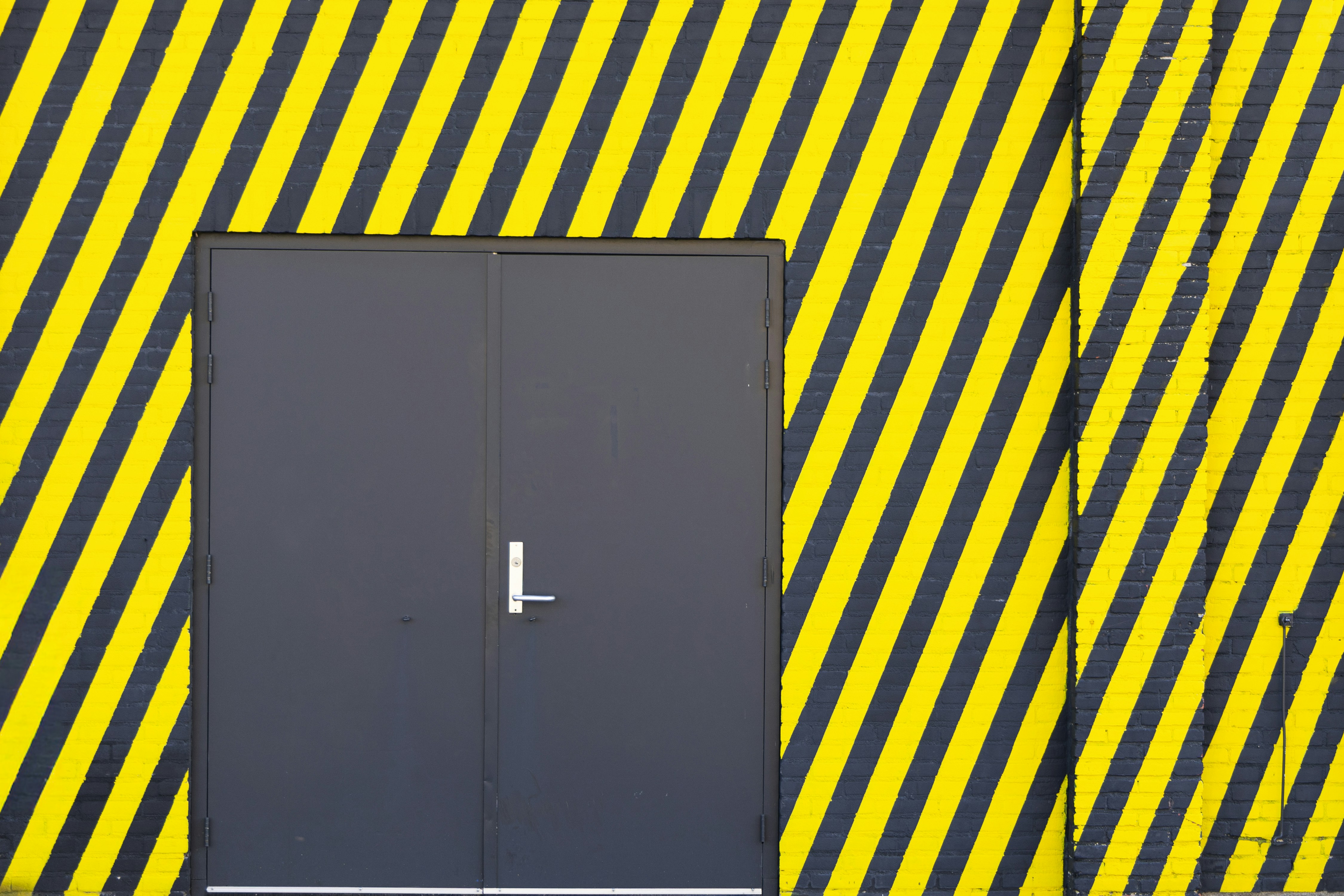 Dark grey door on a yellow and black striped wall.