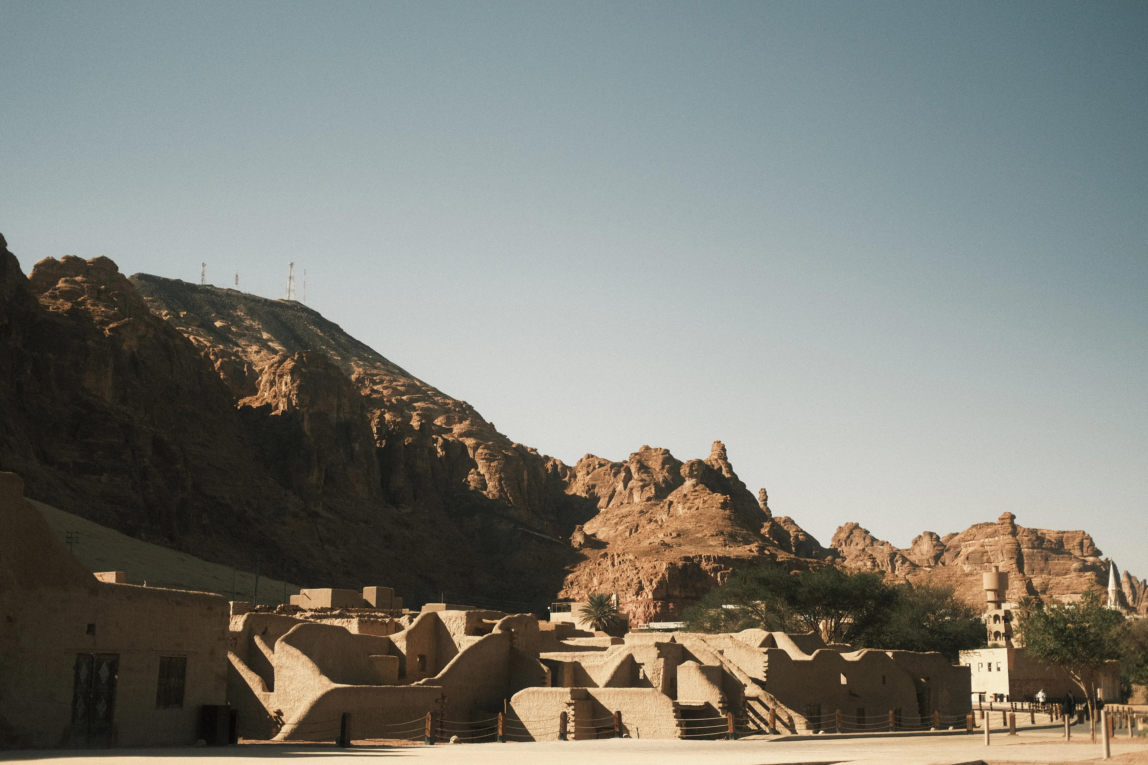 AlUla's restored Old Town citadel of sand-colored buildings set against a rocky mountain backdrop under clear sky.