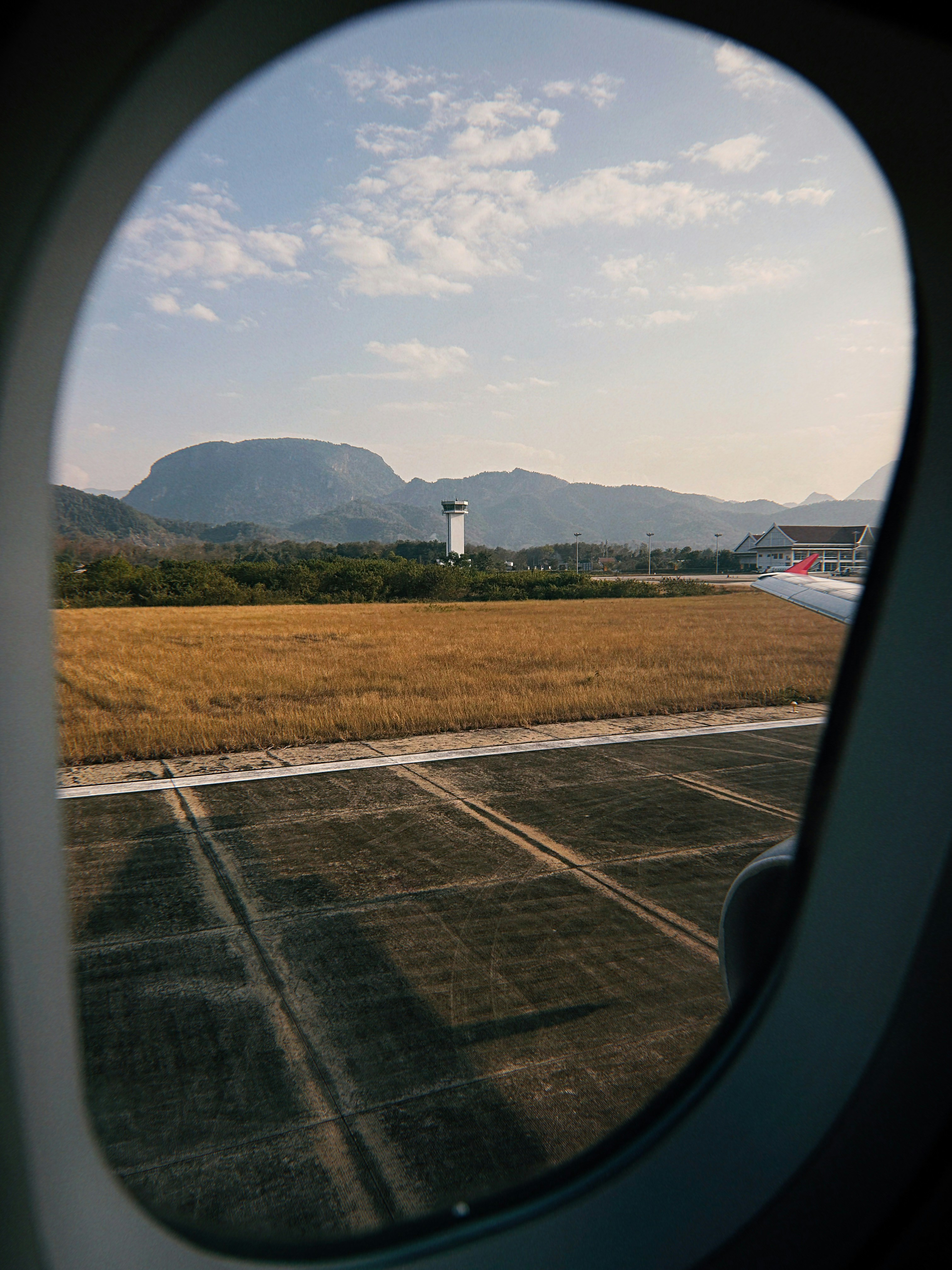 Airplane window view of runway, golden field, and distant mountains.