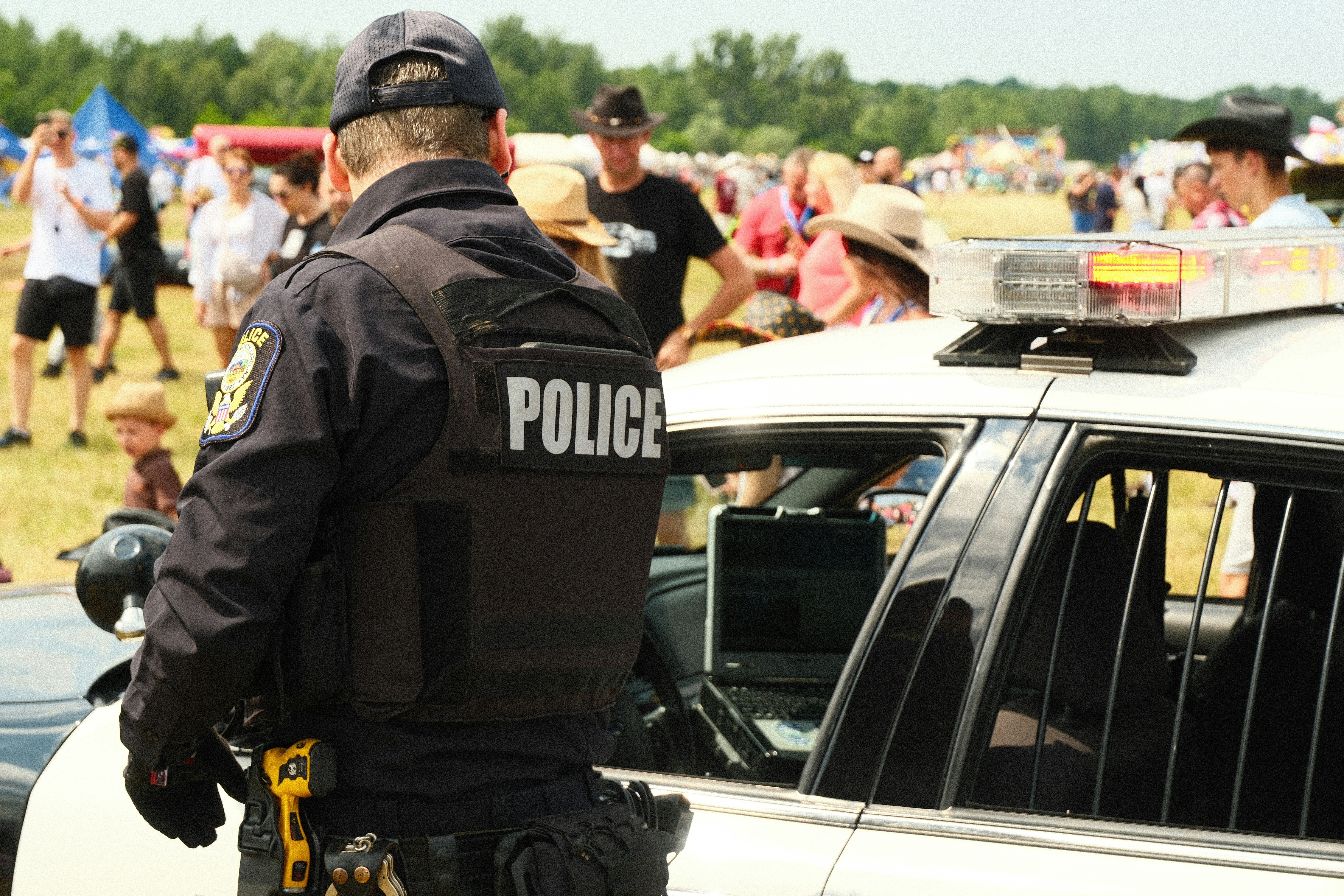 law enforcement officer tactical vest gear - Police officer stands by patrol car at outdoor event.